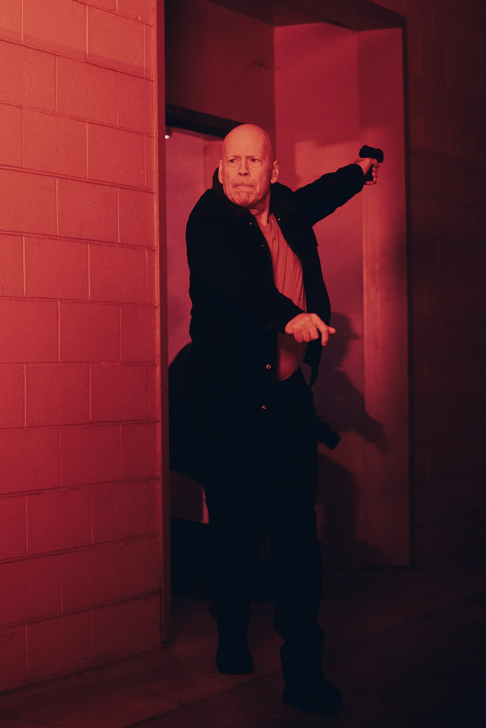 Person in a dimly lit hallway holding a gun with a serious expression.