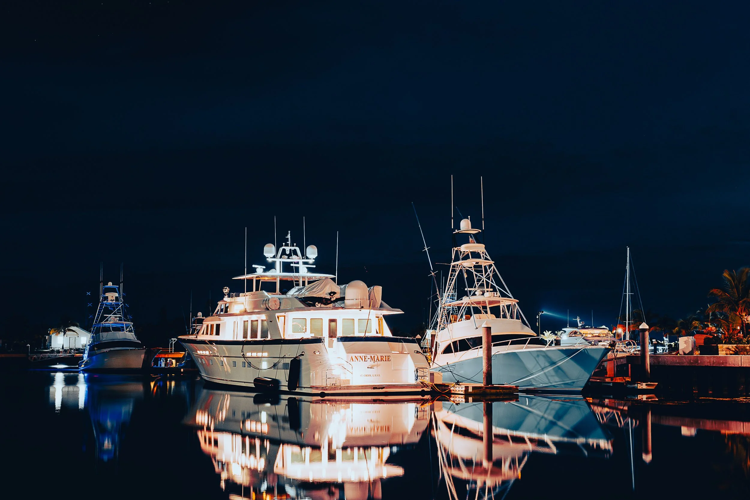 Luxury yachts docked at night with reflections on the water.
