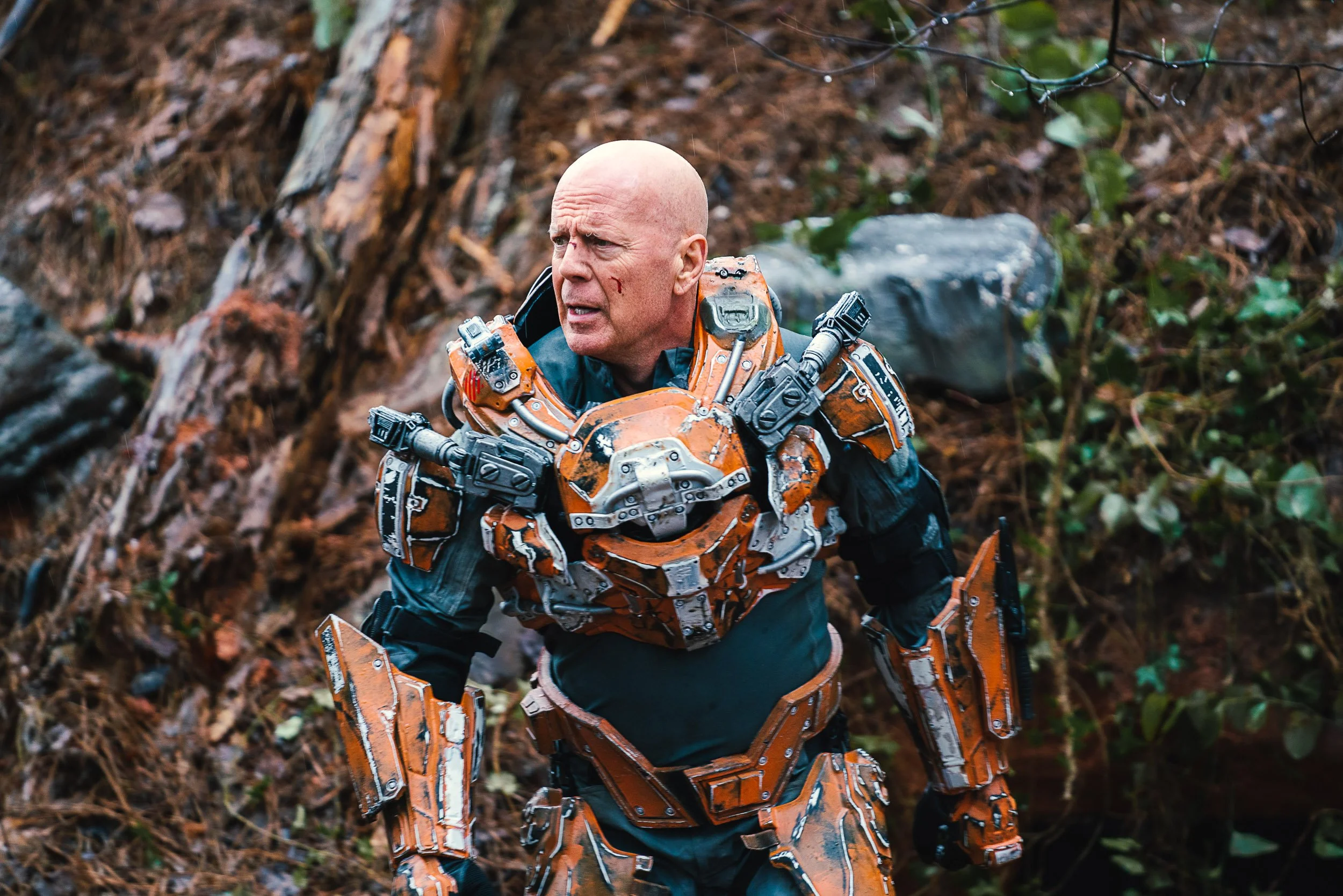 Person wearing orange and silver futuristic armor in a forest setting.