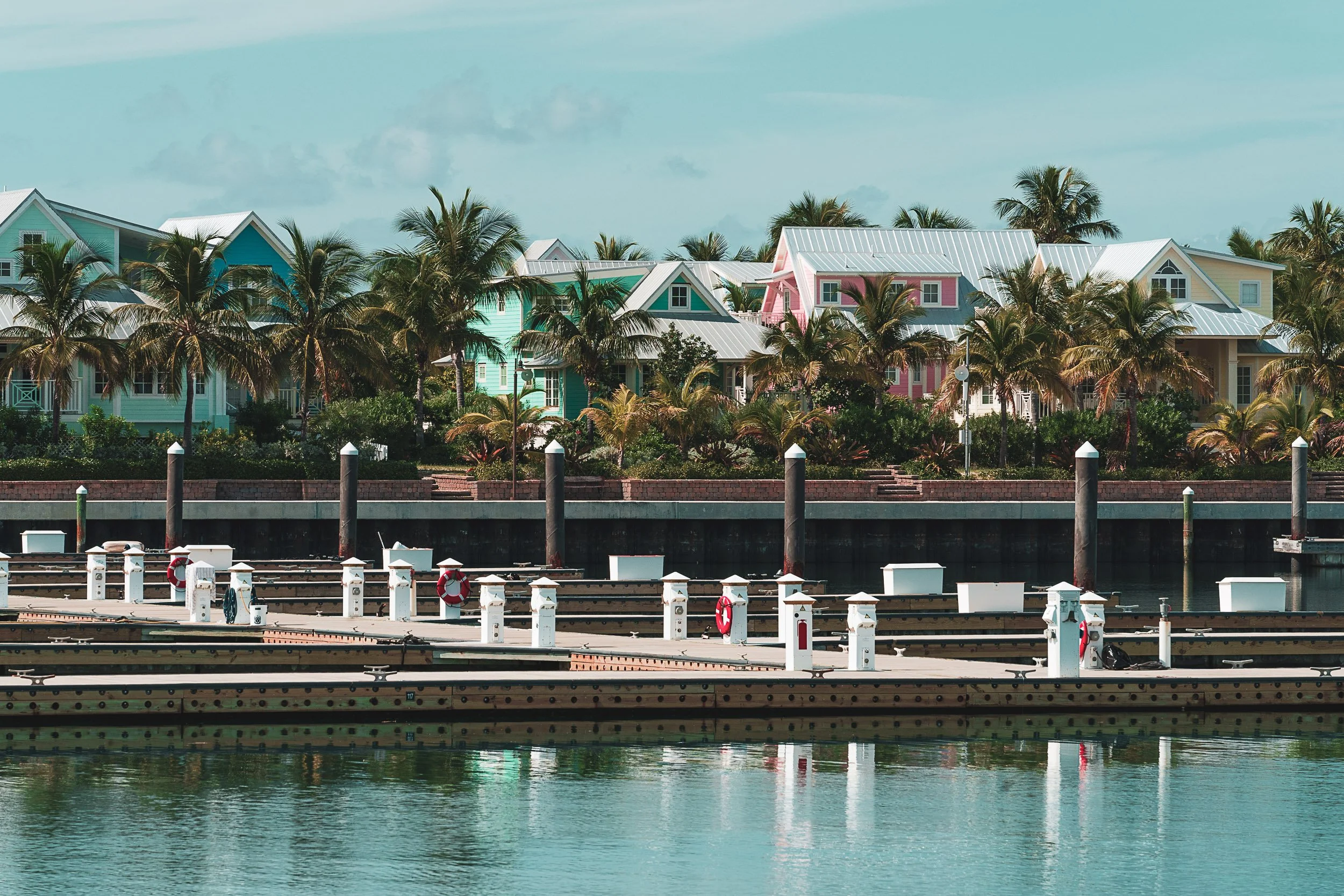 Tropical marina with colorful houses, palm trees, and empty docks.