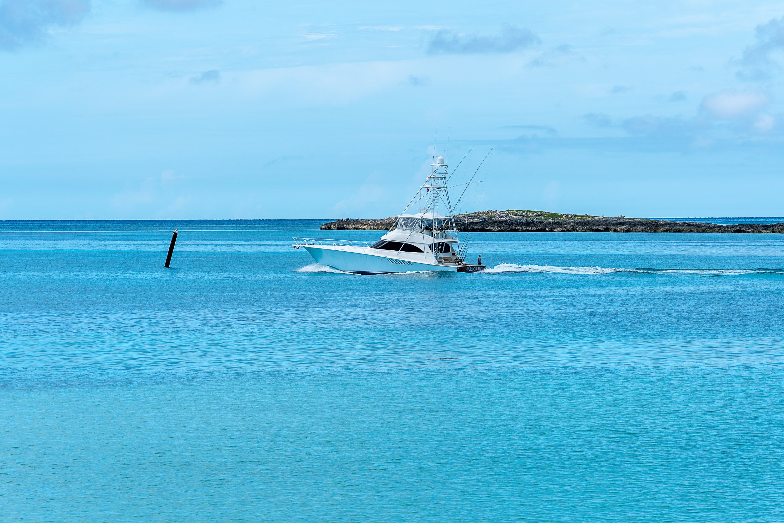 A yacht sailing on clear blue ocean water with an island in the background under a partly cloudy sky.