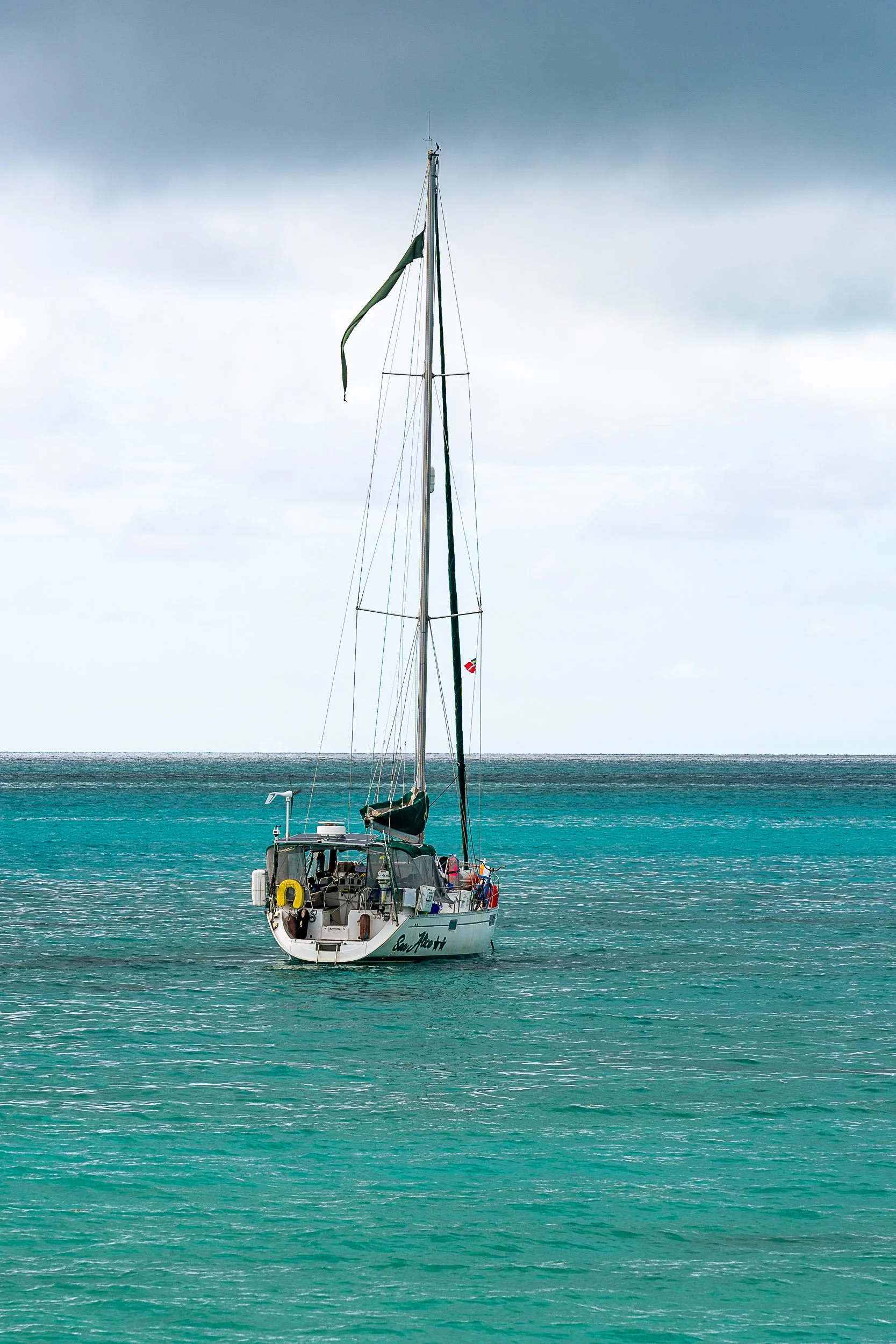 Sailboat floating on turquoise ocean with cloudy sky