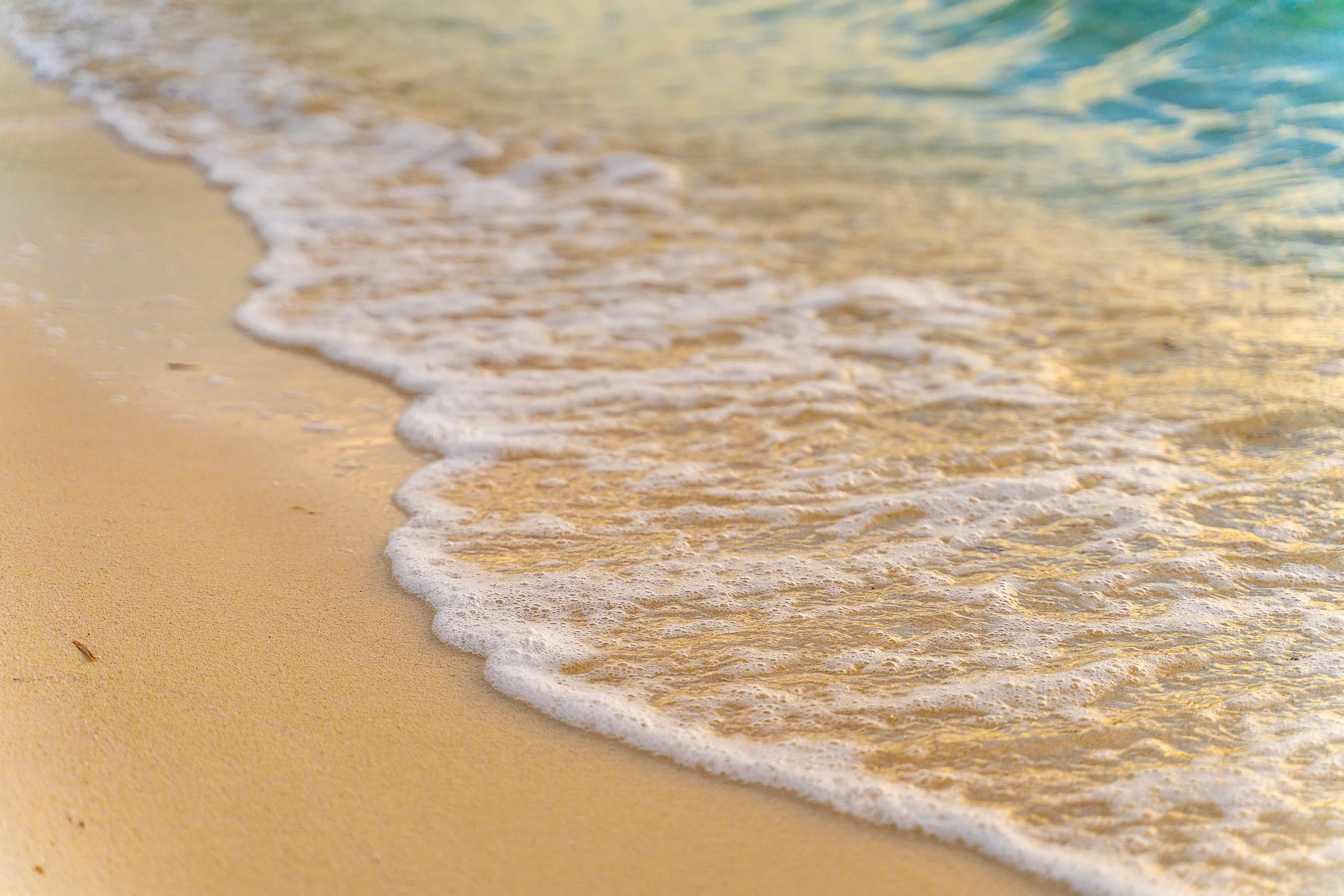 Gentle waves on a sandy beach with sunlight reflections.