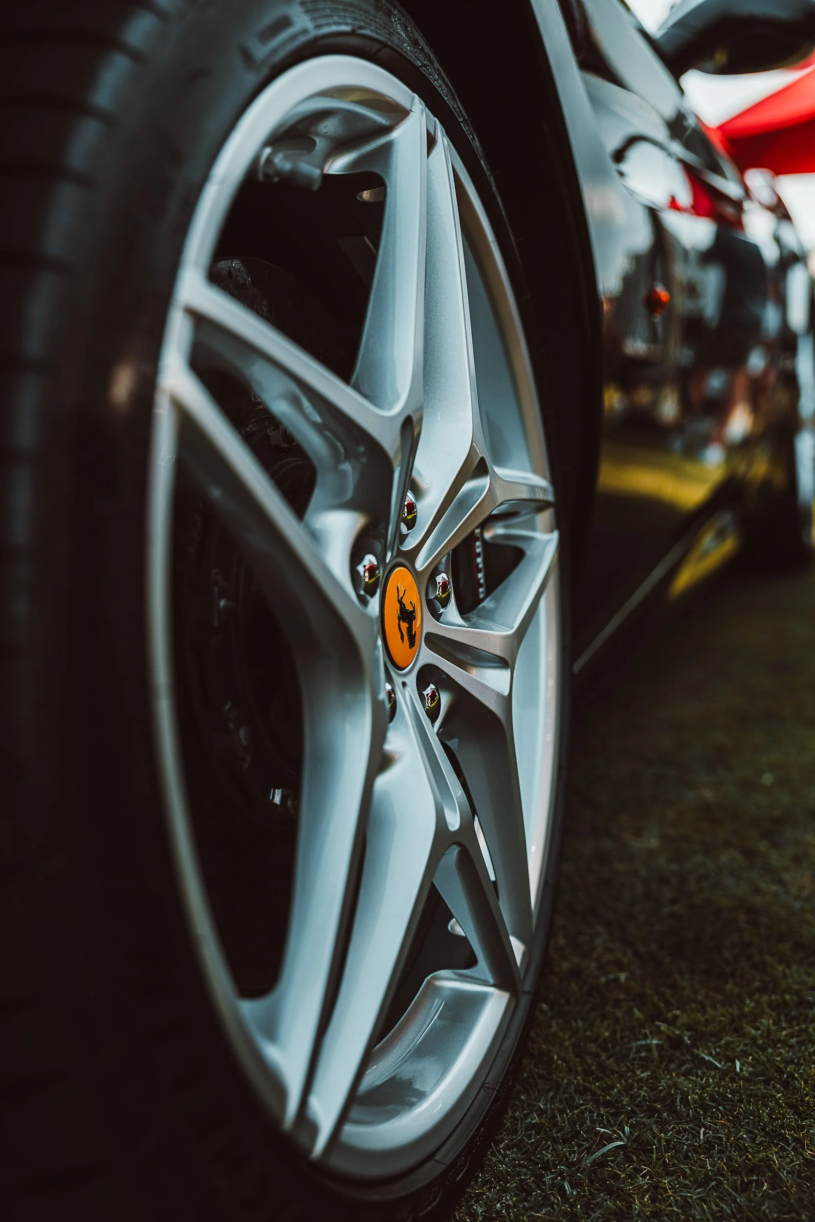 Close-up of a silver car wheel with a yellow logo center cap on grass.