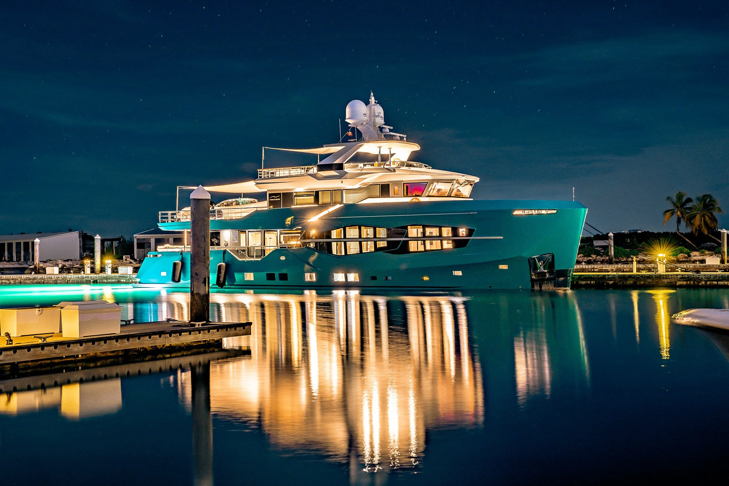 Luxury yacht illuminated at night, docked at a marina with reflections on the water.