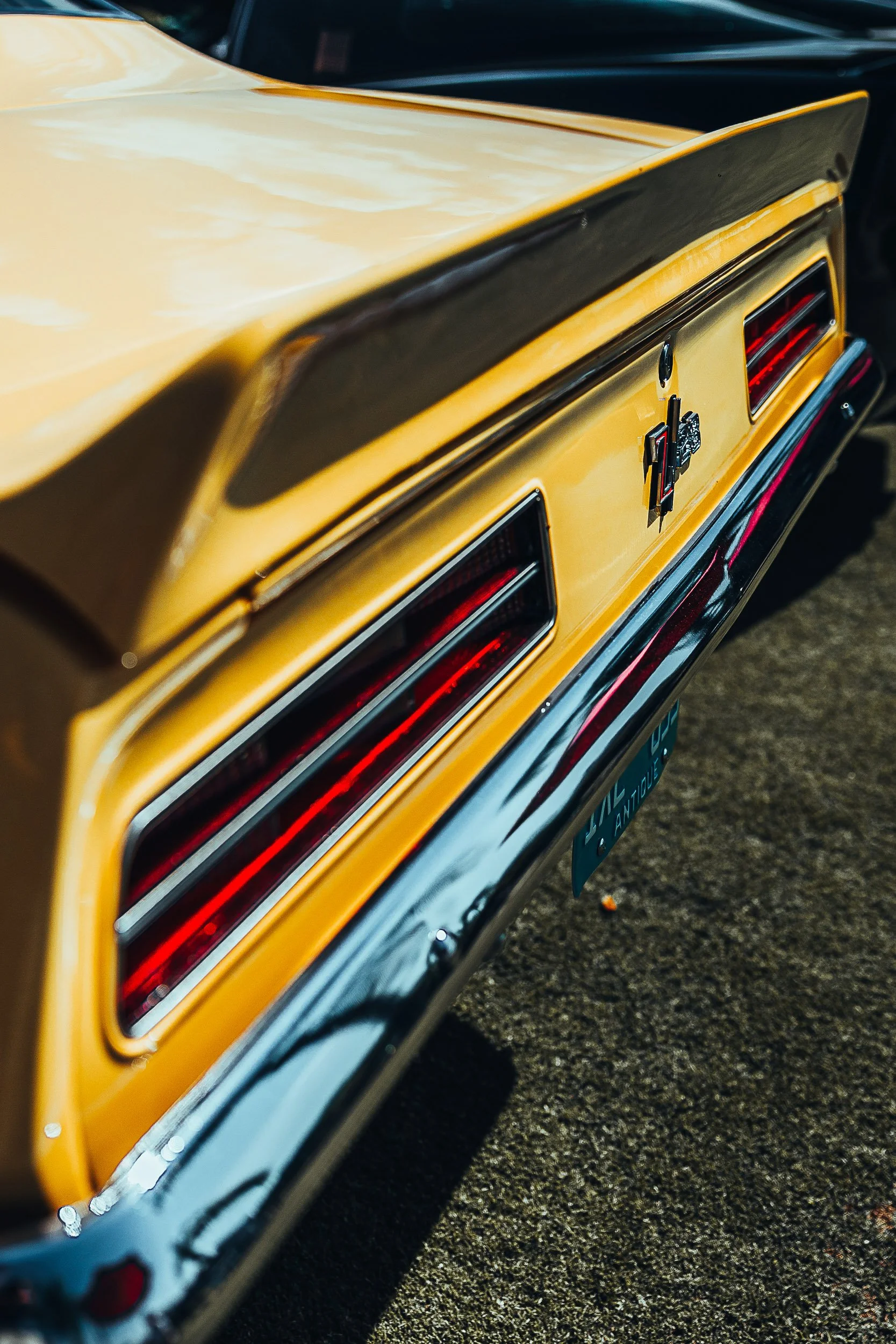 Rear view of a yellow vintage car with chrome bumper and dual rectangular tail lights, featuring an "SS" badge.