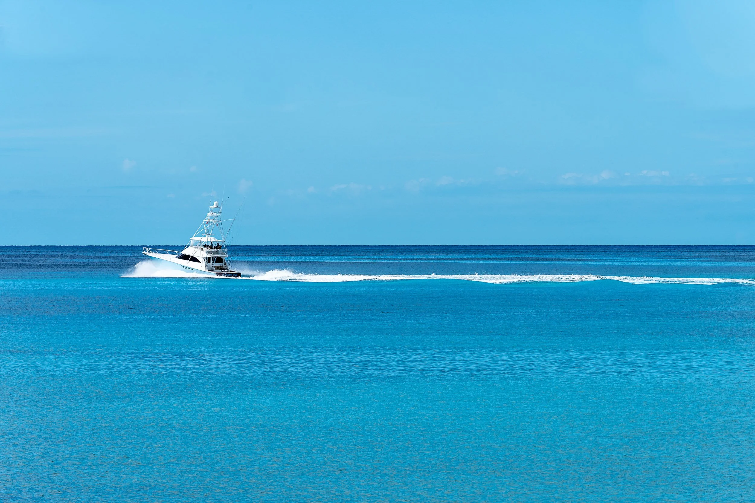 A yacht sailing on clear blue ocean water under a bright blue sky.