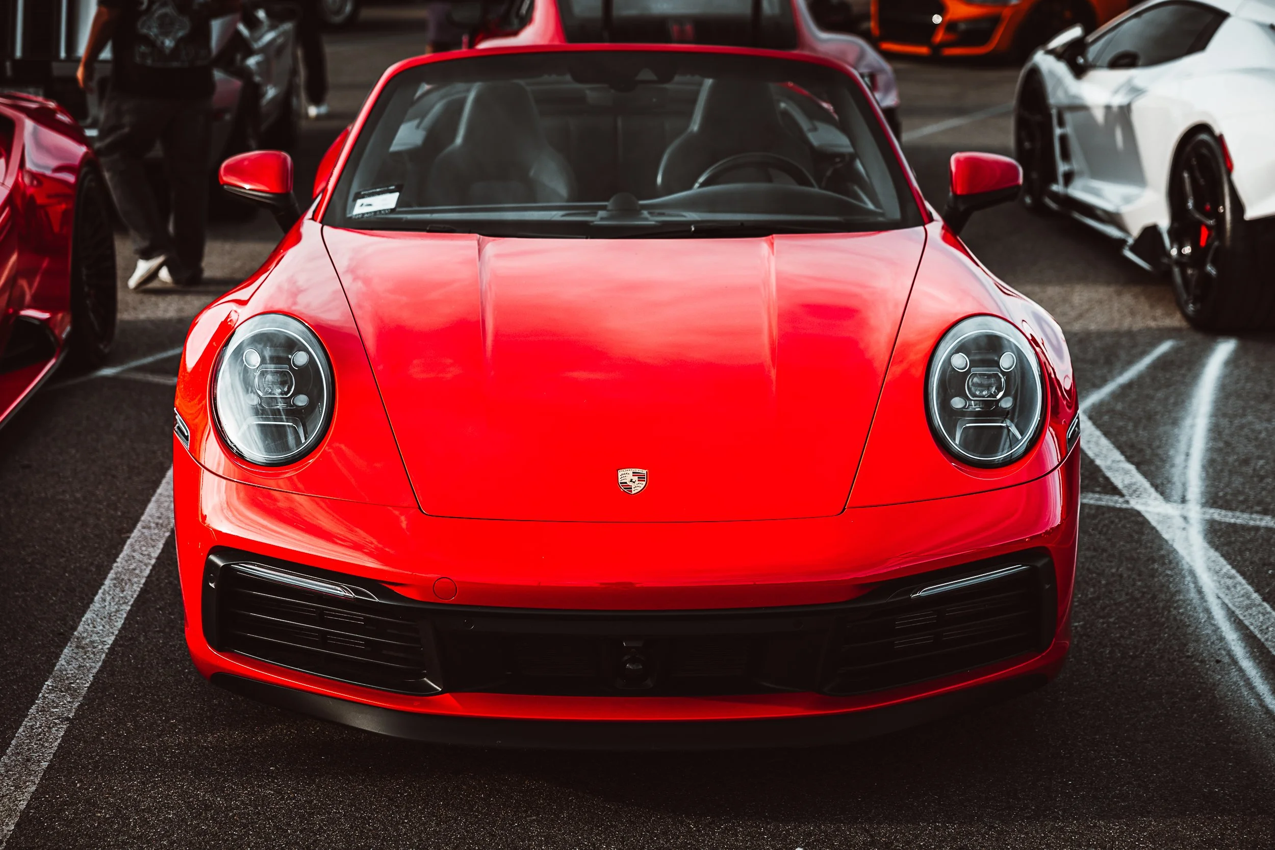 Red Porsche sports car parked in a lot, with other cars visible around it.