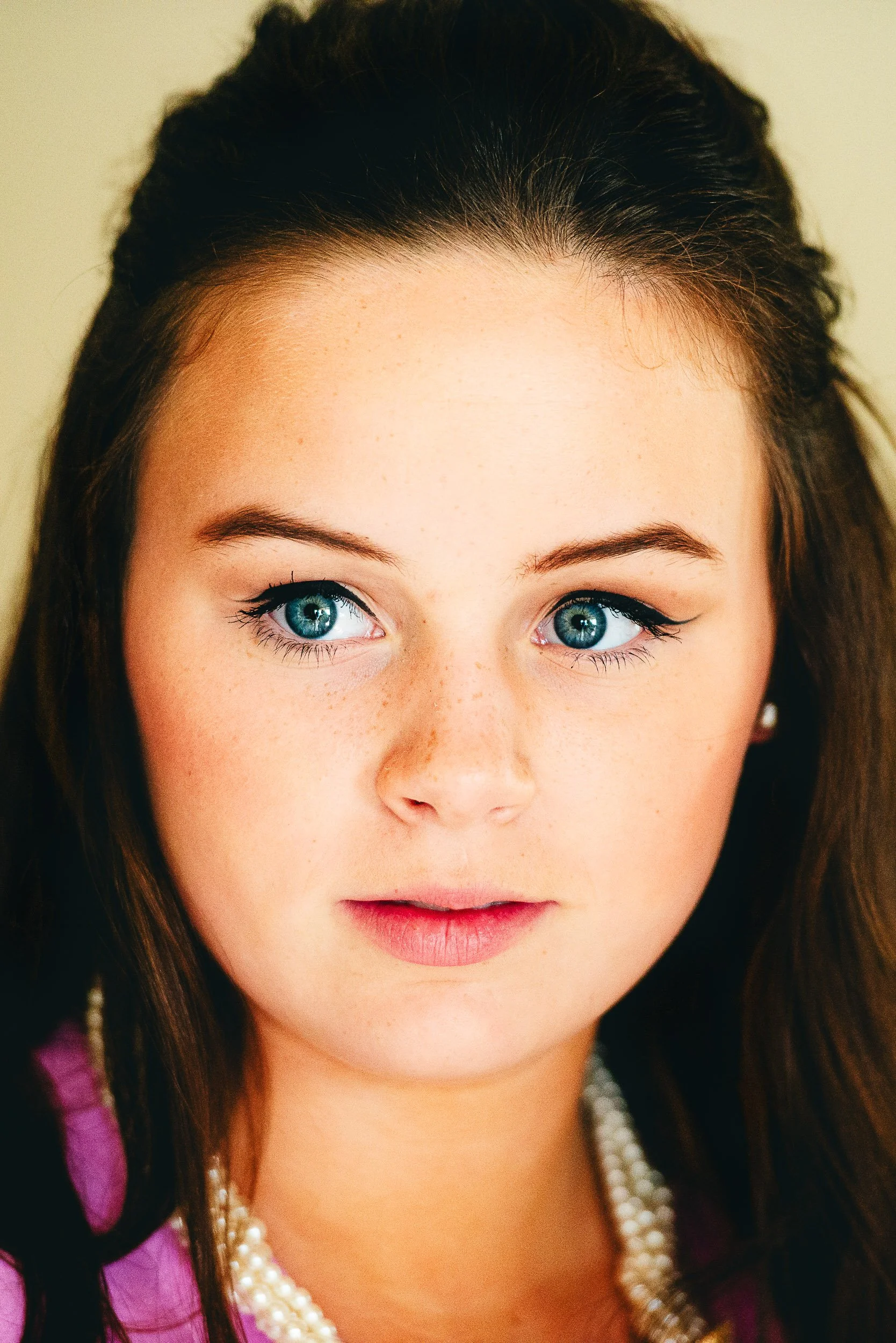 Close-up of a woman with blue eyes, dark hair, and a pearl necklace, looking to the side.