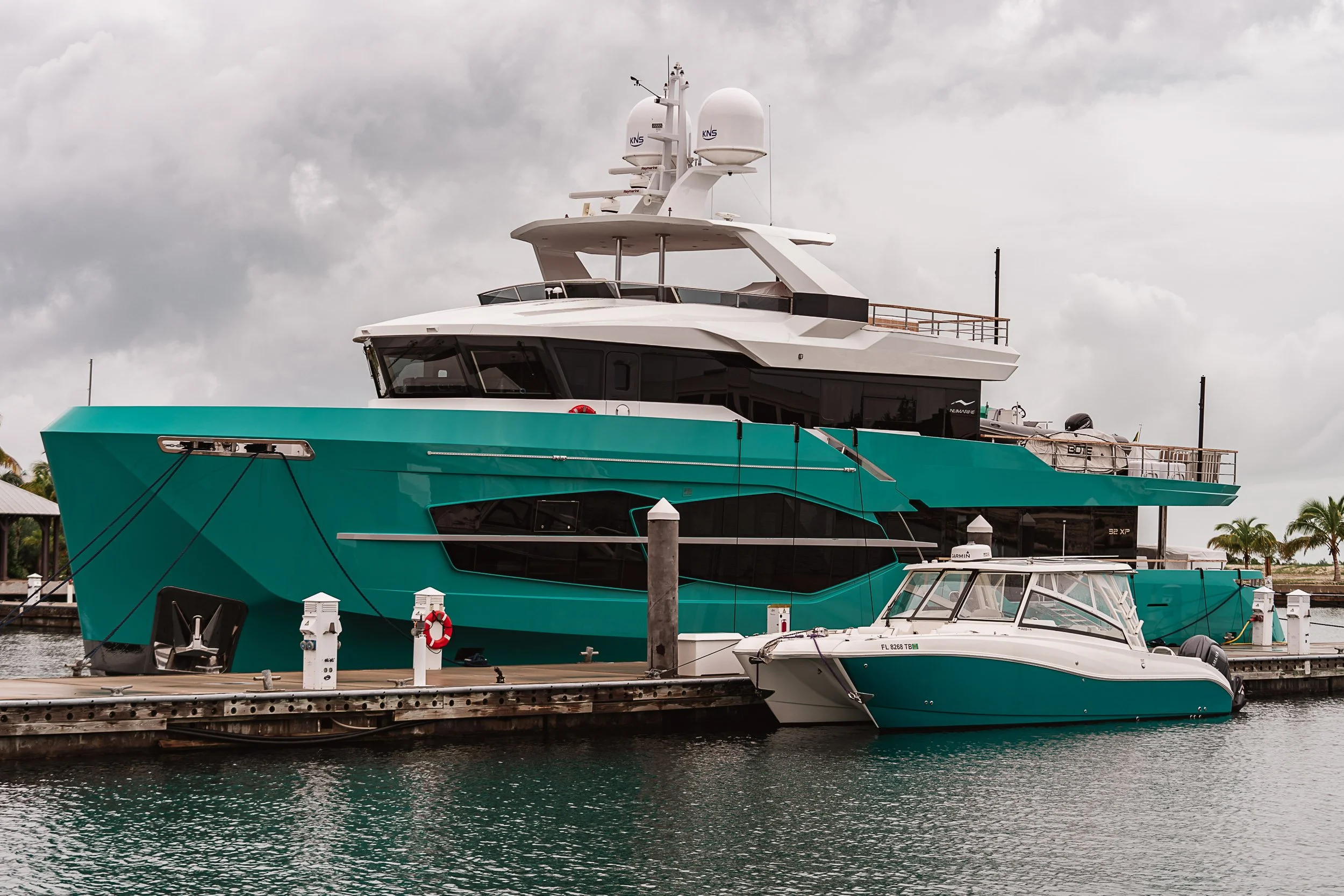 Luxury turquoise yacht docked at marina with overcast sky.