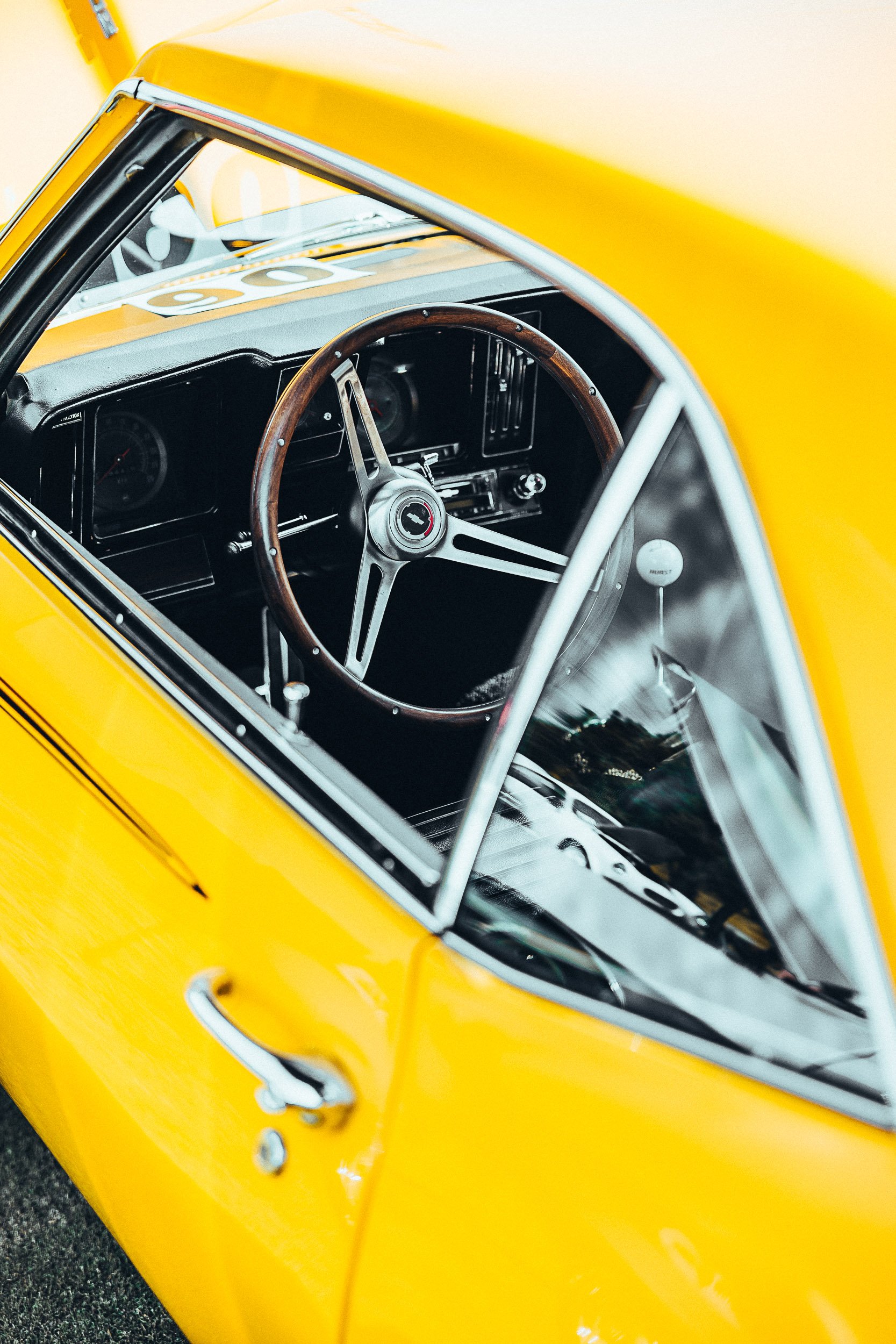 Interior view of a yellow vintage car focusing on the steering wheel and dashboard through the window.