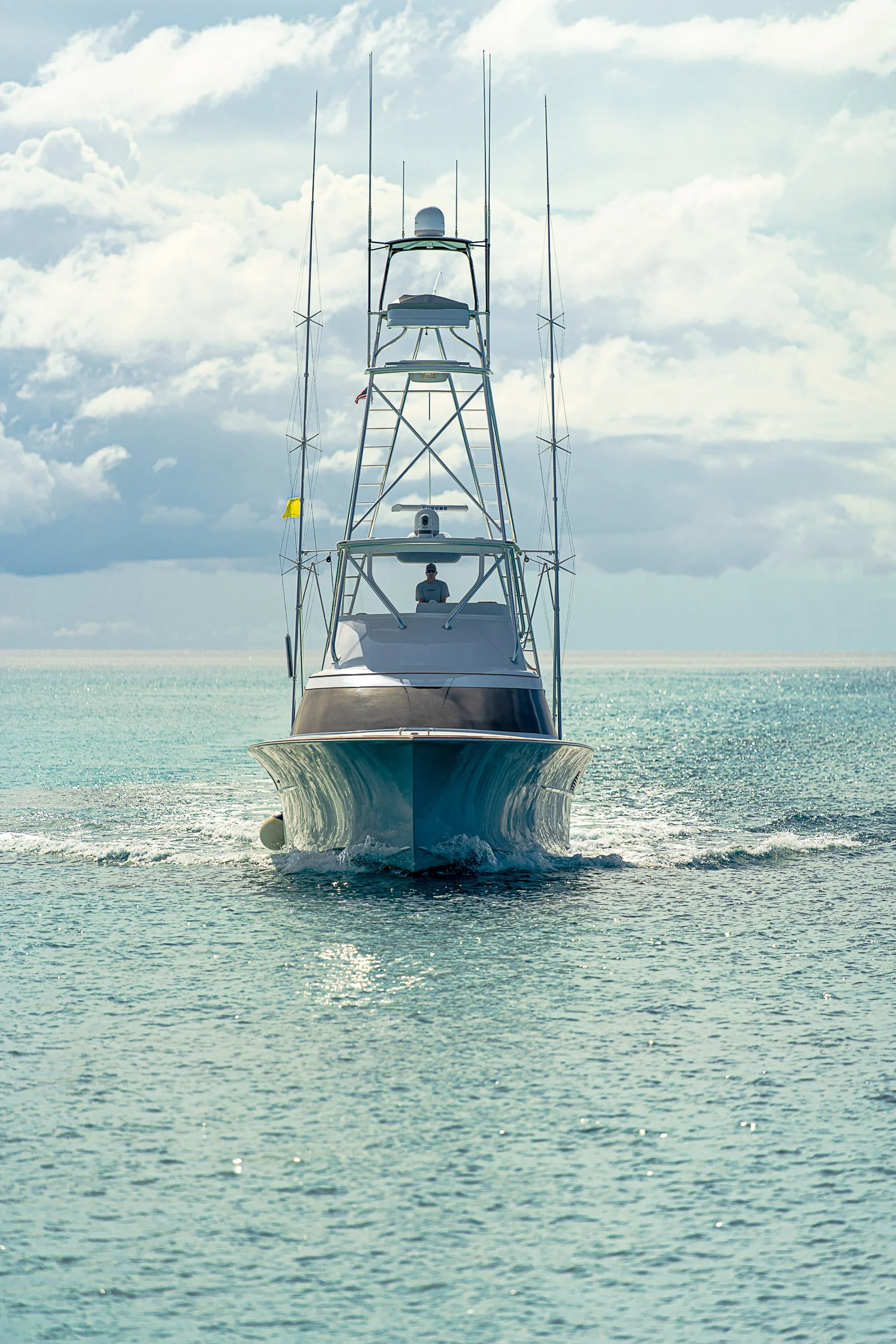 Front view of a sport fishing boat with multiple antennas on the open sea under cloudy skies.