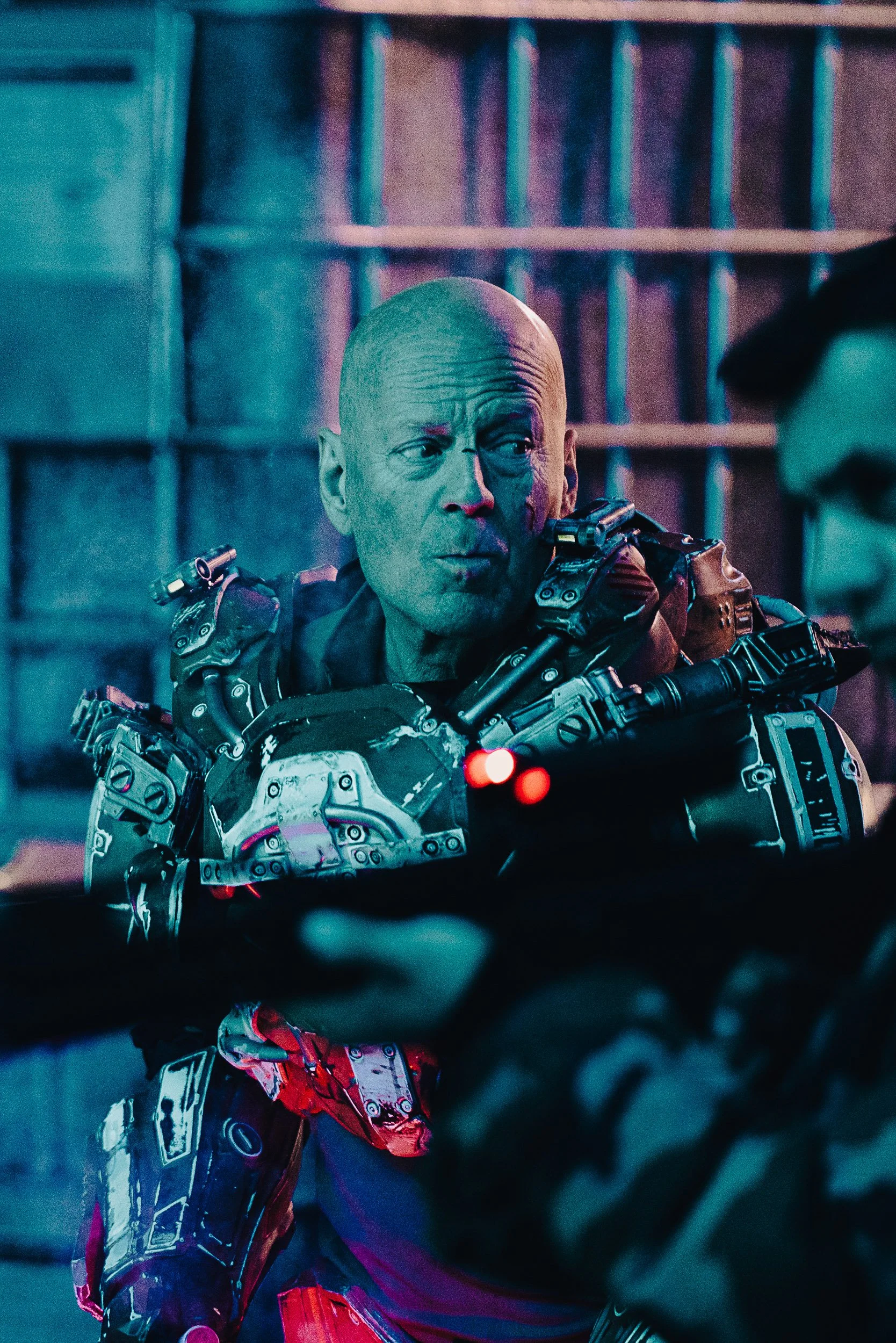 A person wearing futuristic armor inside a sci-fi setting, with another person in camouflage holding a weapon close by.