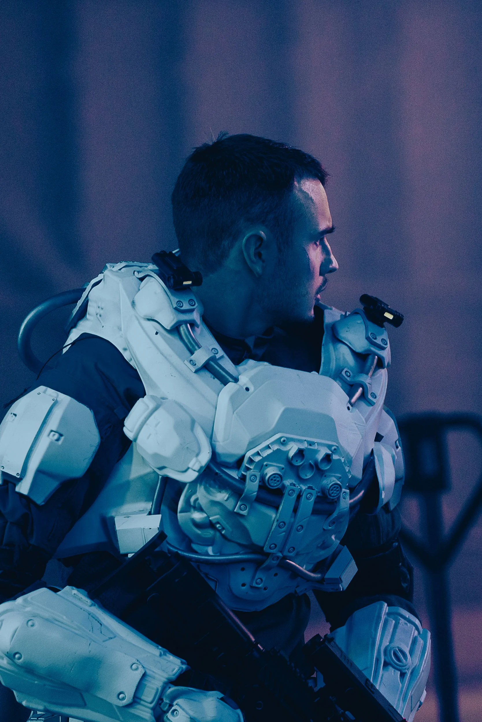 Person wearing futuristic armor with technological elements, dark background.