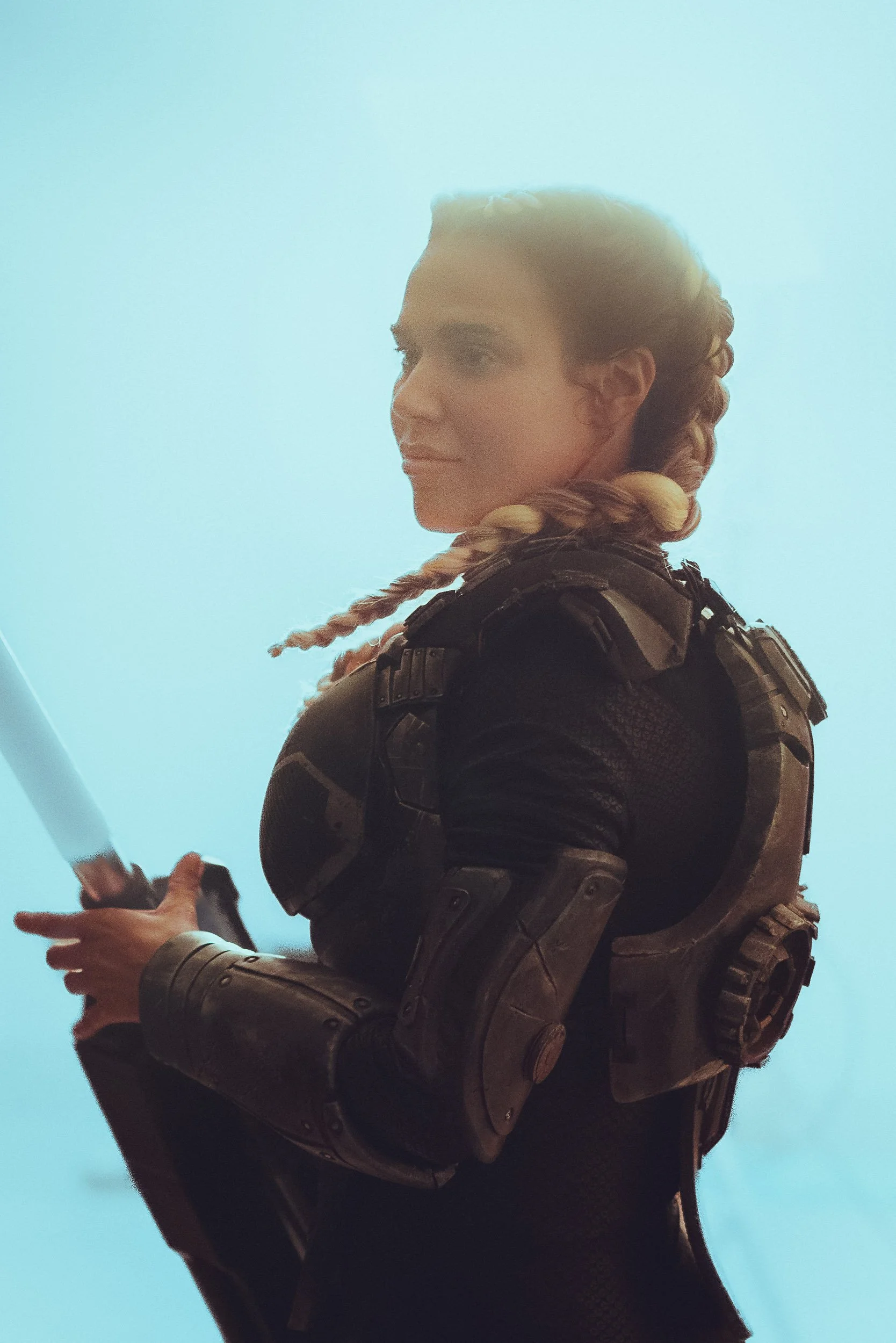 Woman in futuristic armor holding a large weapon, with braided hair, against a blue background.