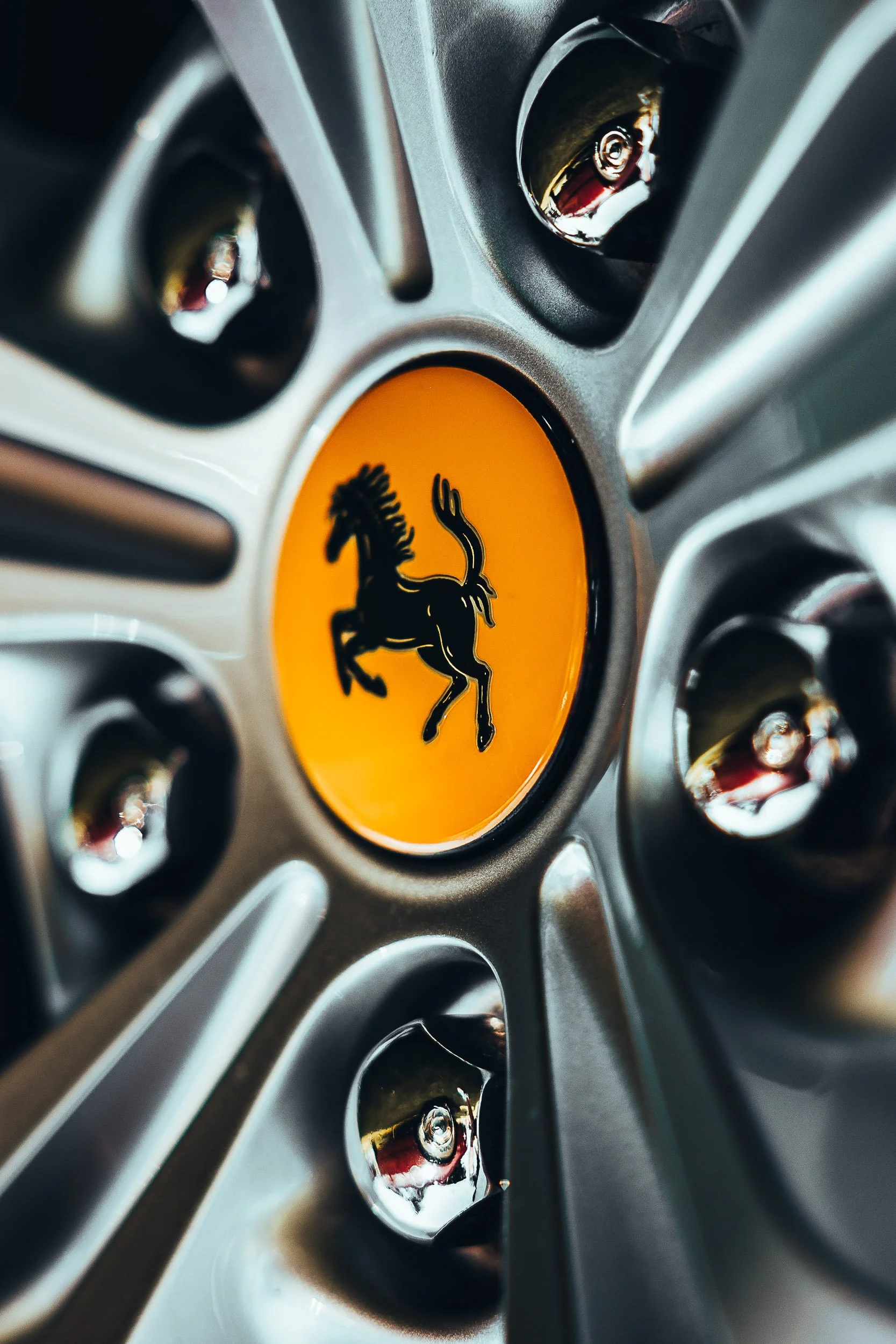 Close-up of a car wheel hub featuring a prancing horse logo, surrounded by chrome lug nuts.