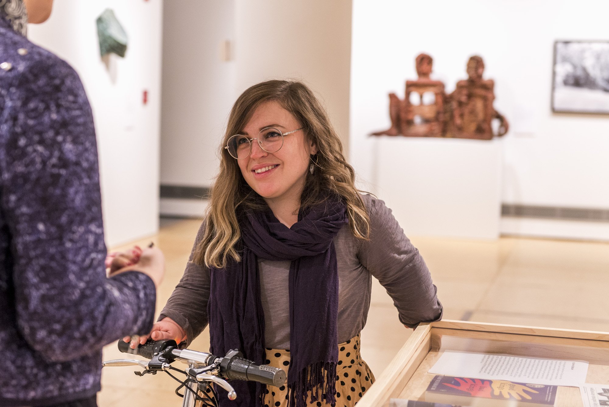 Bri sits on her mobility scooter in an art gallery and faces an interviewer asking her questions.
