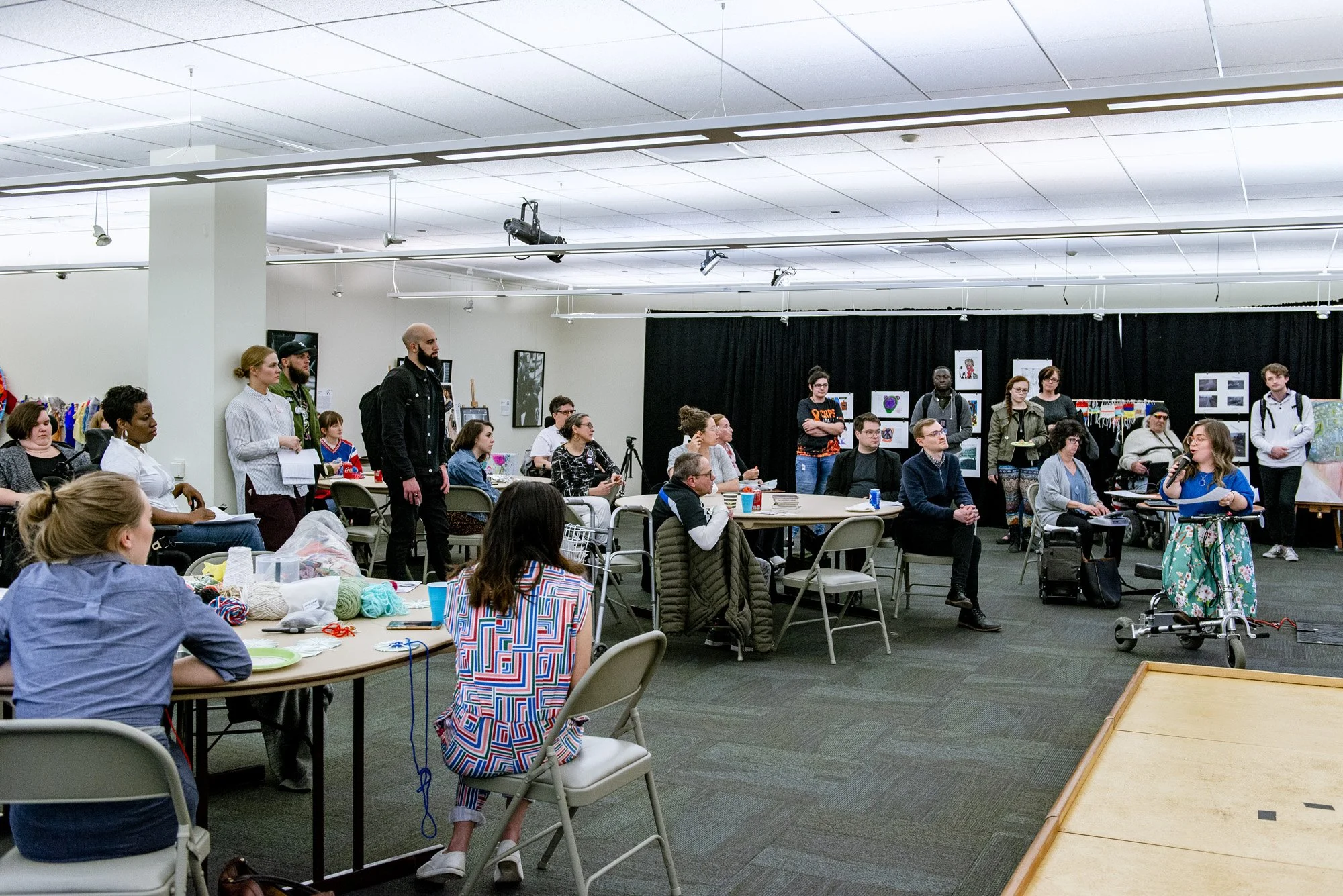 Bri sits on her mobility scooter and addresses a large crowd at a community event.