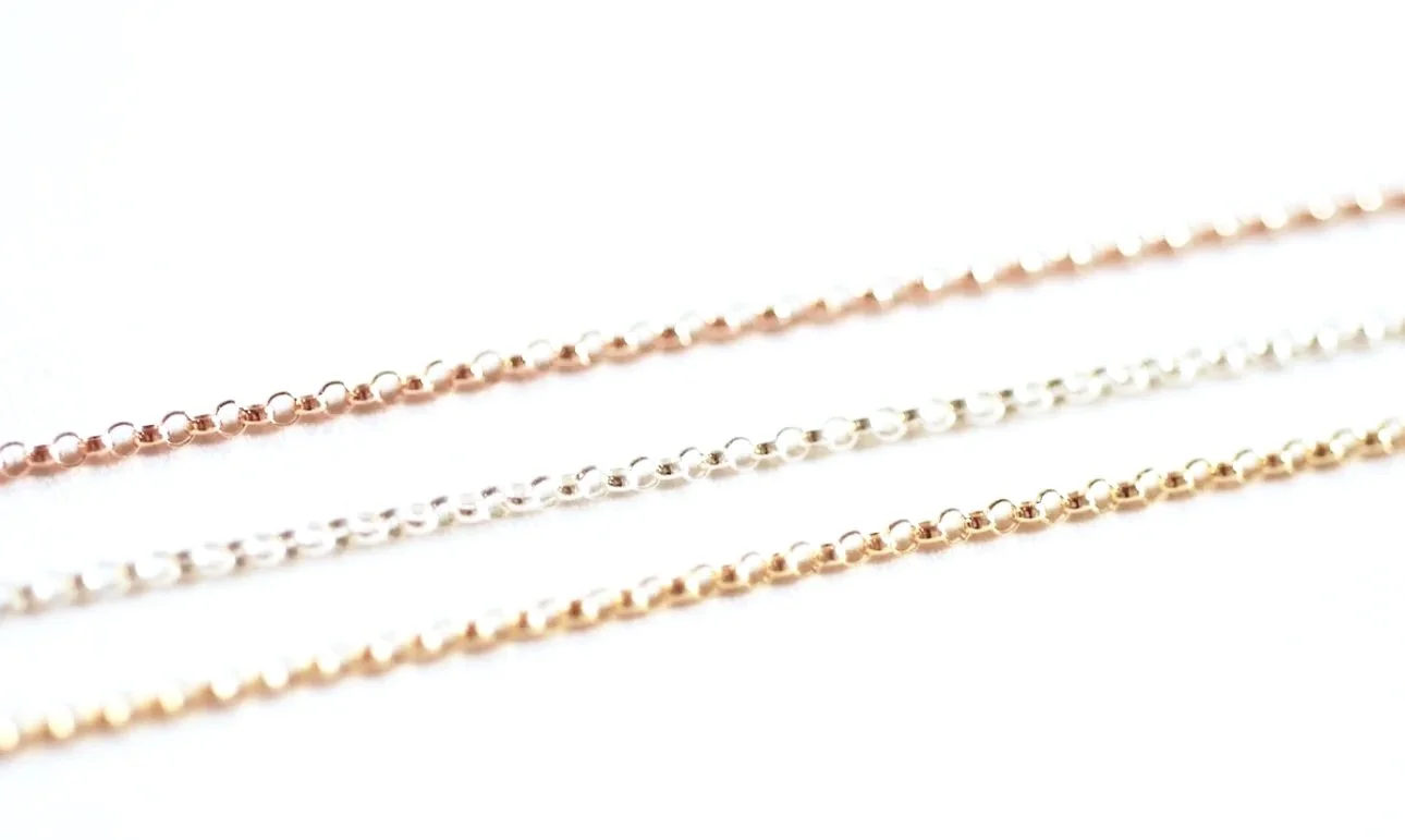 Close-up of four delicate, gold, silver, and rose gold beaded chains laid out on a white surface.