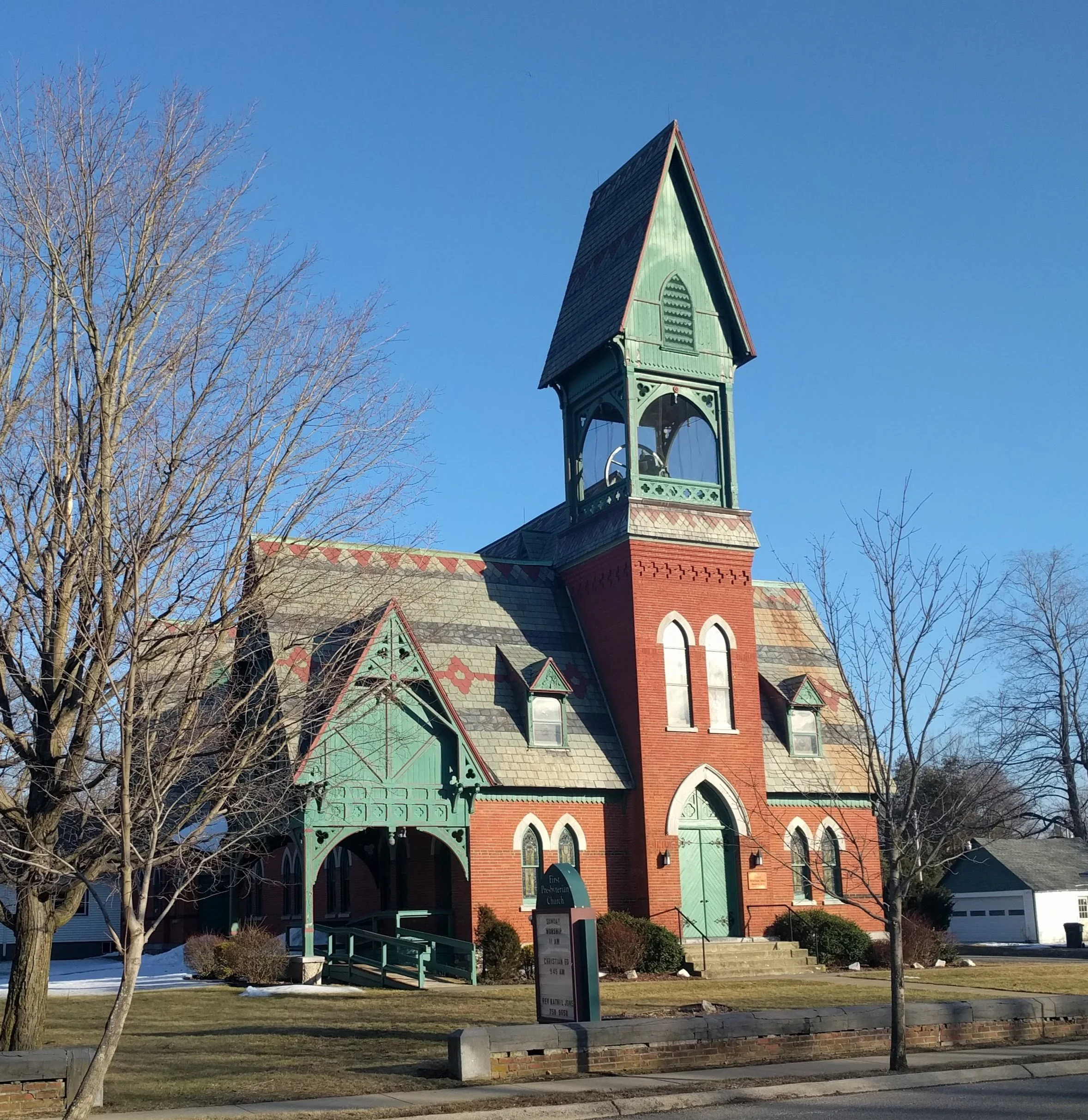 A historic church with a tall steeple and Gothic windows, surrounded by leafless trees, on a sunny day.