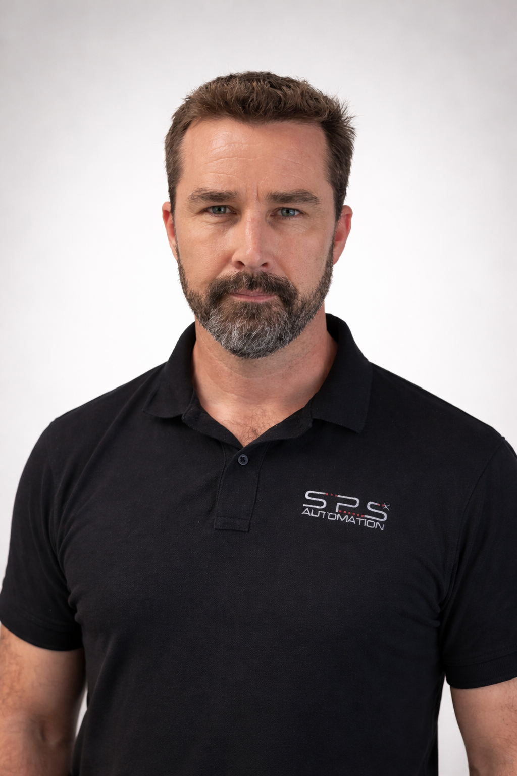 A middle-aged man with brown hair and a beard, wearing a black polo shirt with the logo 'SPS Automation,' standing against a plain white background.