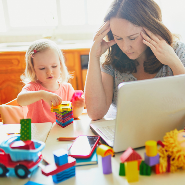 Busy mum working on a laptop while caring for her young child at home