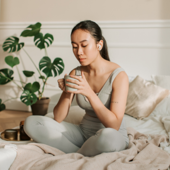 Woman sitting comfortably on a bed, holding a cup of tea and enjoying a quiet moment to herself.