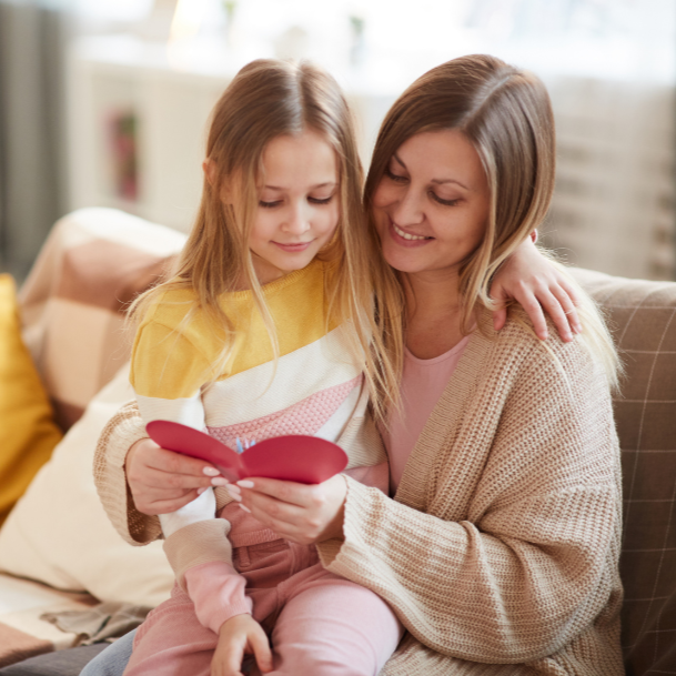 mother hugging daughter while reading heart-shaped card