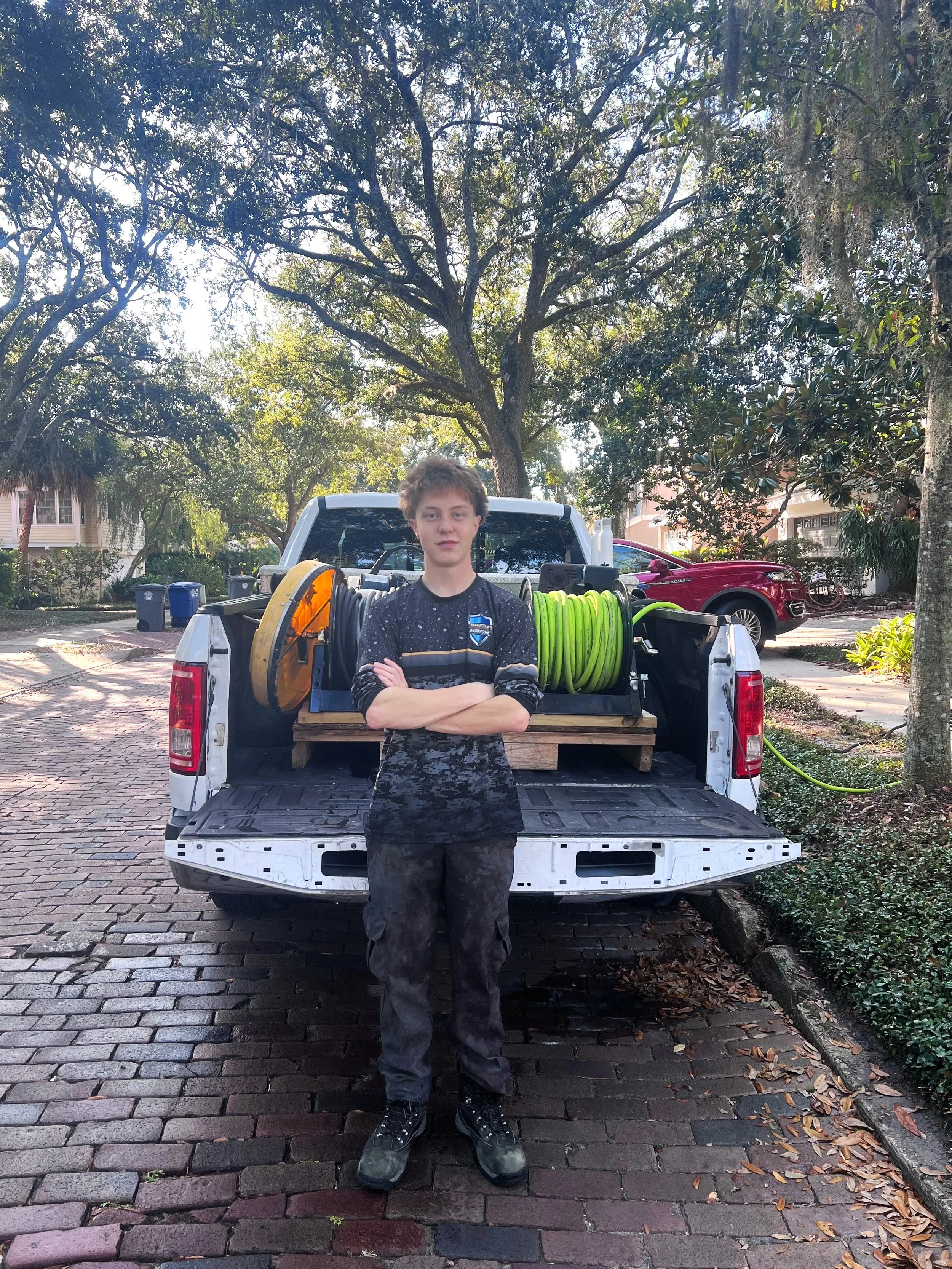 Knight wash technician smiling and standing with arms crossed at the back of a pickup truck with hoses and equipment in the back