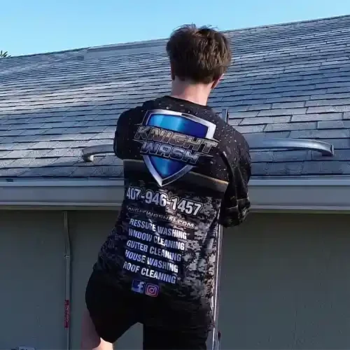 A Knight Wash technician on a ladder cleaning gutters