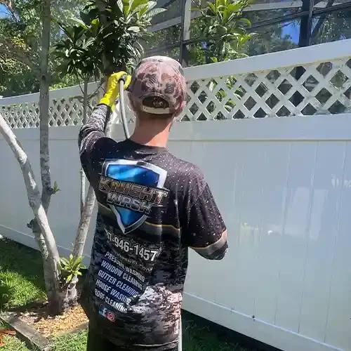 A Knight Wash technician spraying a cleaning solution to remove organic material on a Orlando white vinyl fence.