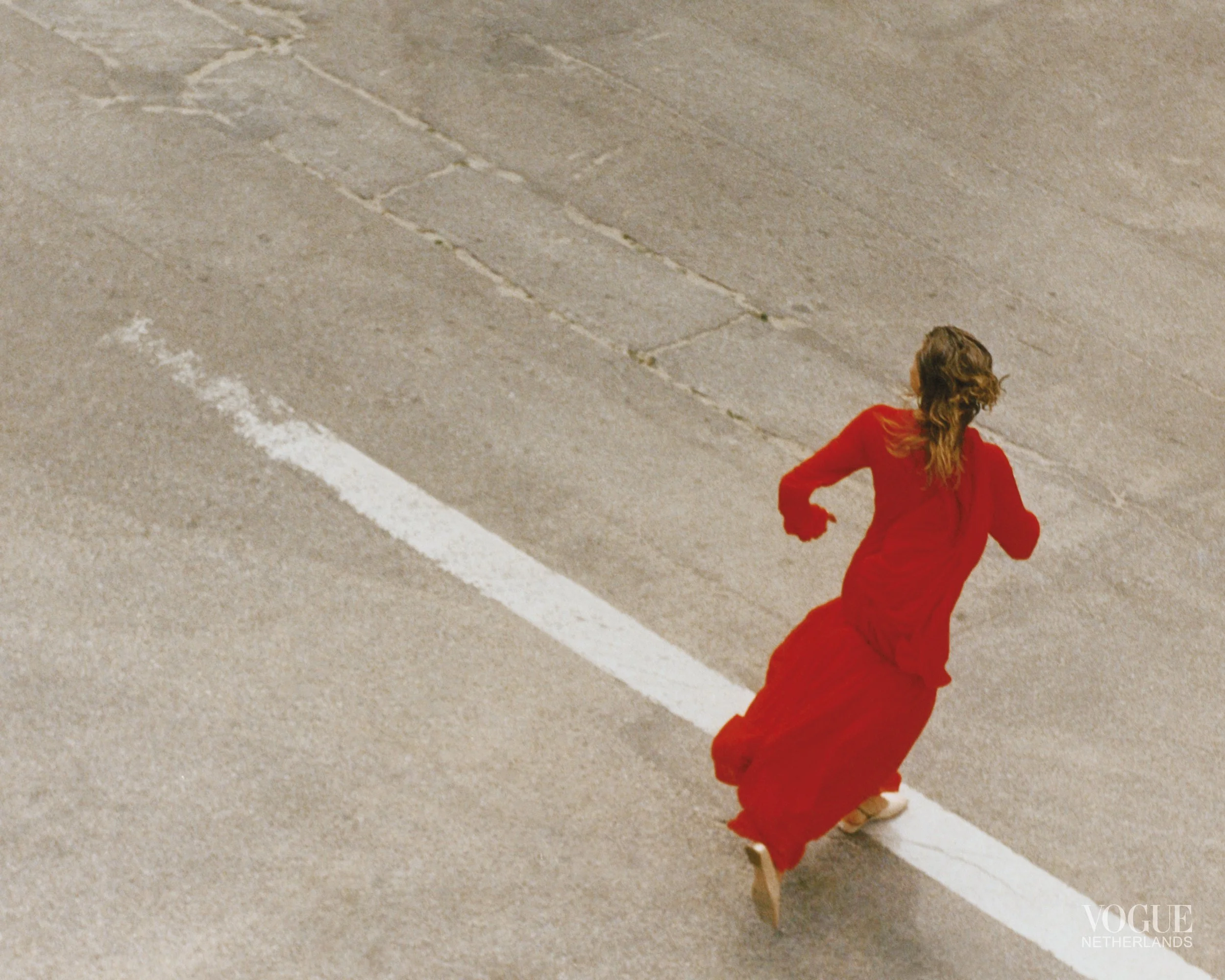 Woman in a long red dress walking along a marked white line on an empty street.