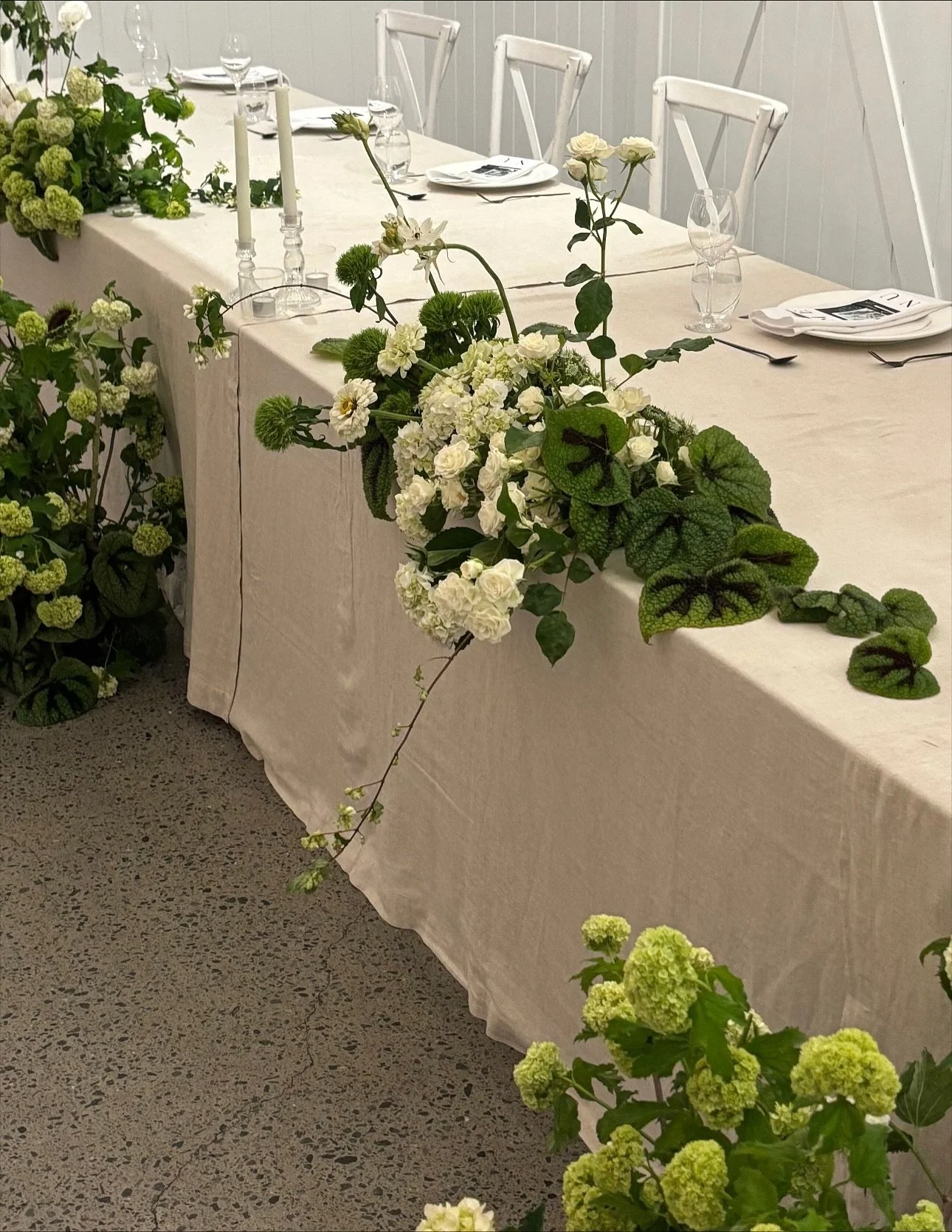 Megan &amp; Wade choose their bridal table to be the main feature of their reception. Guest tables were paired back and kept timeless with white linen and tapered candles. The bridal table, with a warm oat linen and sculptural florals that draped acr