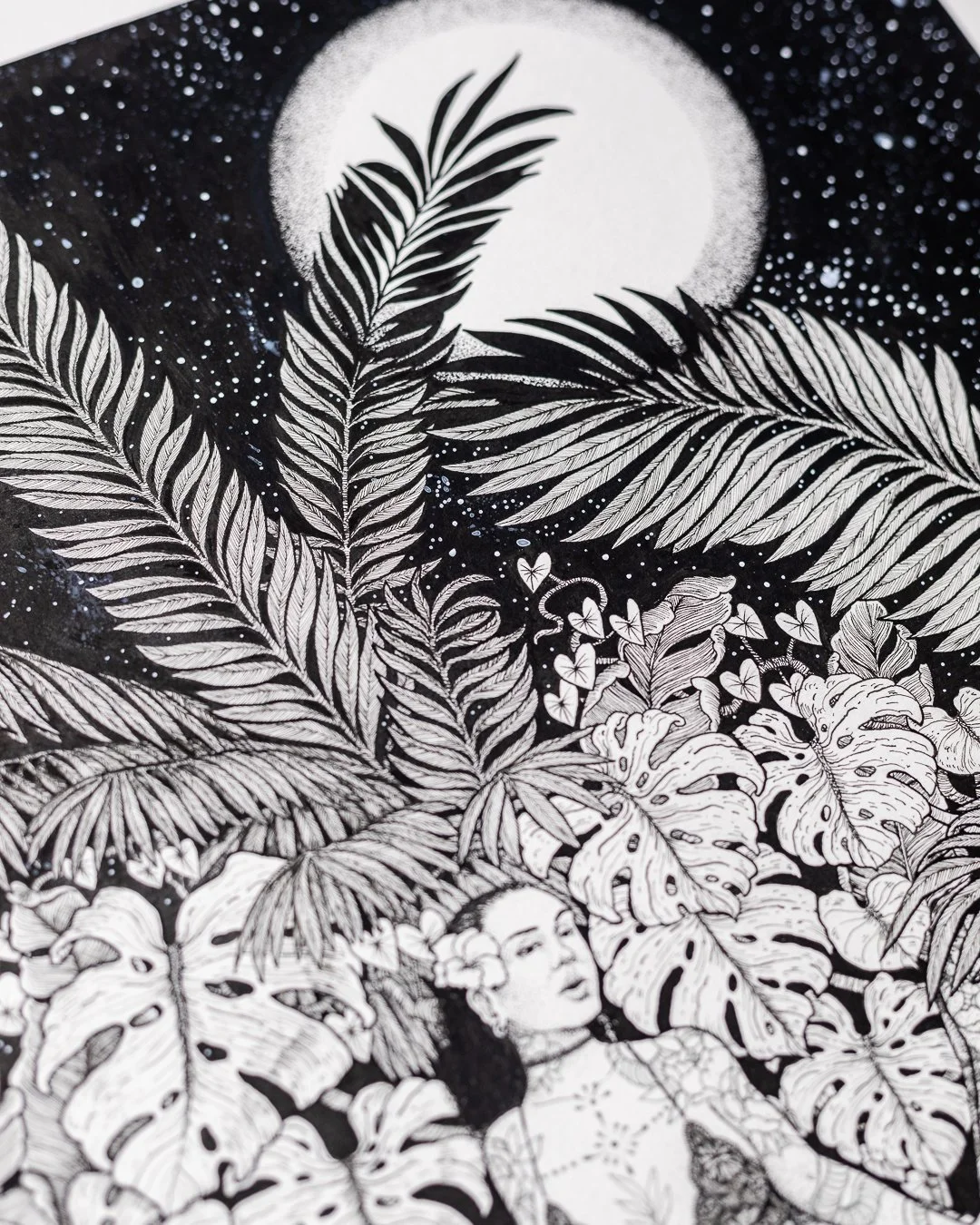 Black and white illustration of lush tropical leaves, a woman with flowers in her hair, and a large full moon in the sky, with stars scattered around.