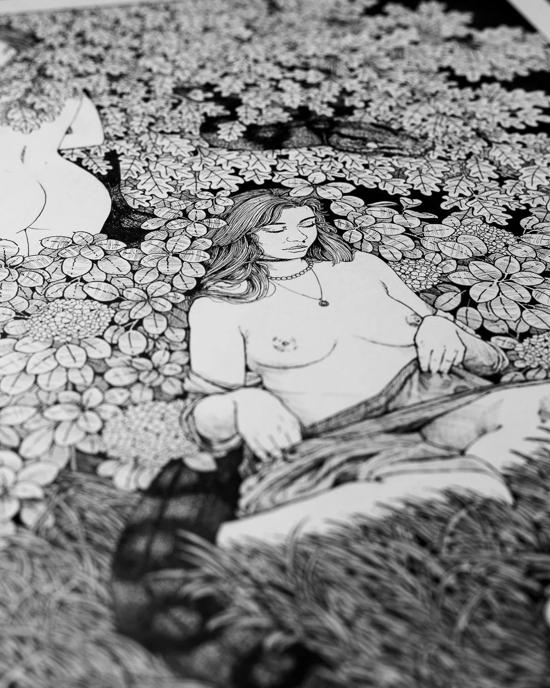 Black-and-white illustration of a topless woman with long hair, sitting and surrounded by leaves and flowers, with her eyes closed.