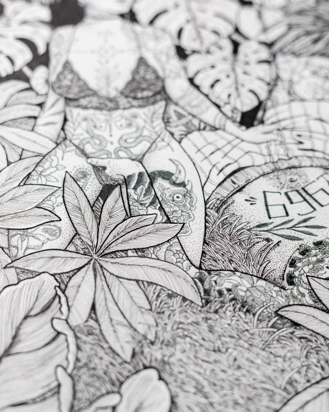Close-up of a detailed black and white illustration featuring leaves, a skull, a snake, and other intricate designs.