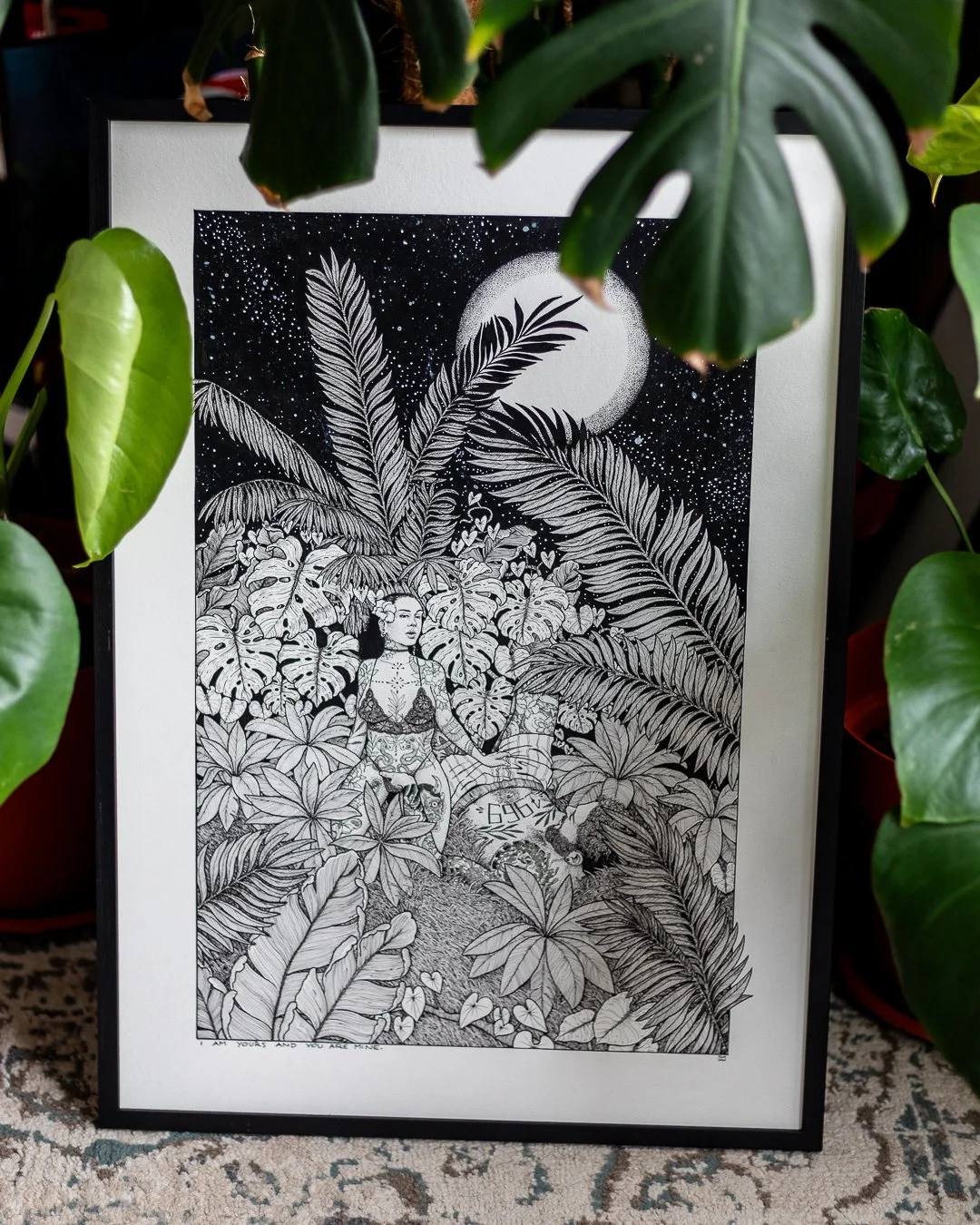 Black and white illustration of a woman standing among lush tropical plants, moon in the night sky, surrounded by large leaves and foliage.