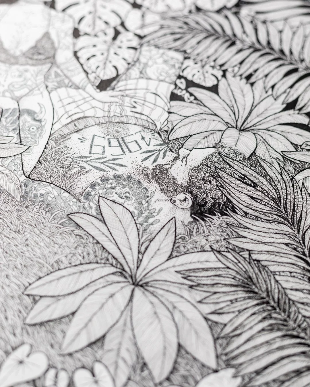 Detailed black and white botanical illustration featuring various tropical leaves and a person with a beard and curly hair, surrounded by dense foliage.
