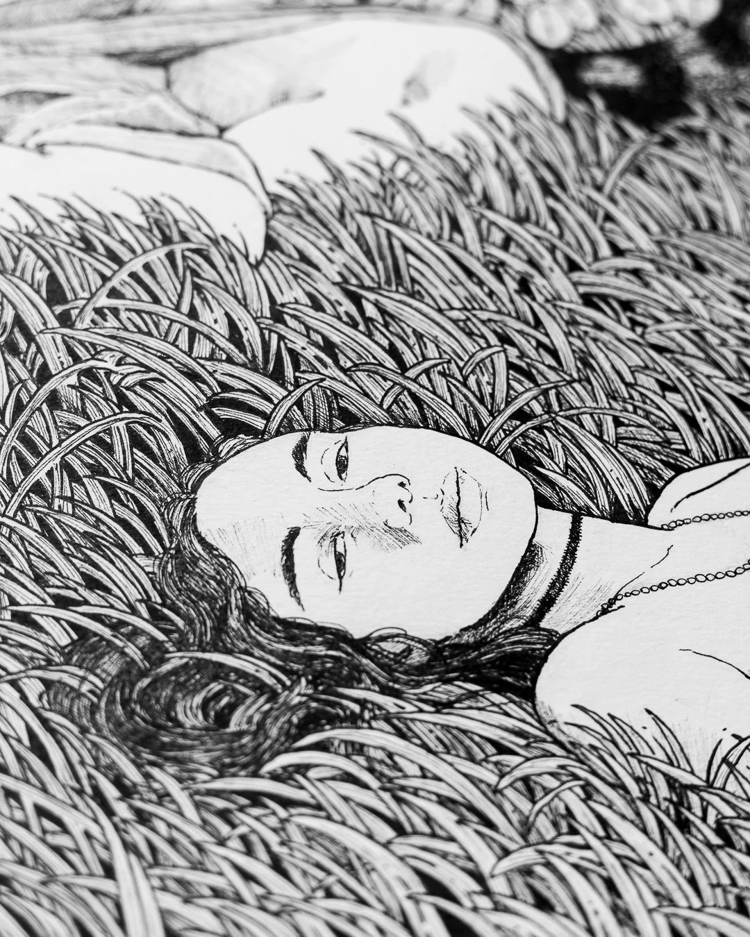 Black and white drawing of a woman lying in tall grass, with her eyes half-closed and long wavy hair spread around her. She is wearing necklaces and has a calm expression.