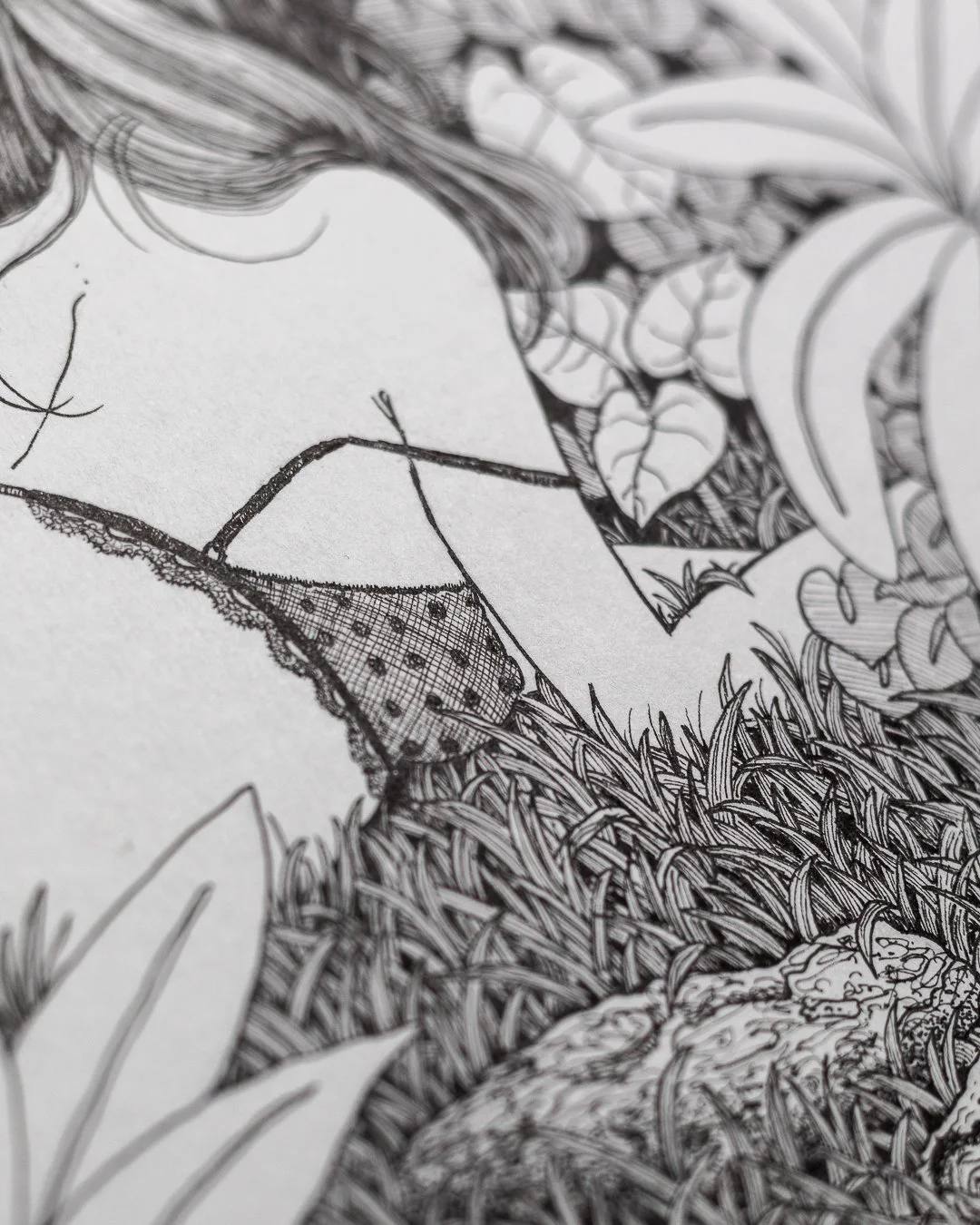 Close-up of a black-and-white line drawing of a woman with long, wavy hair, surrounded by various plants and leaves.