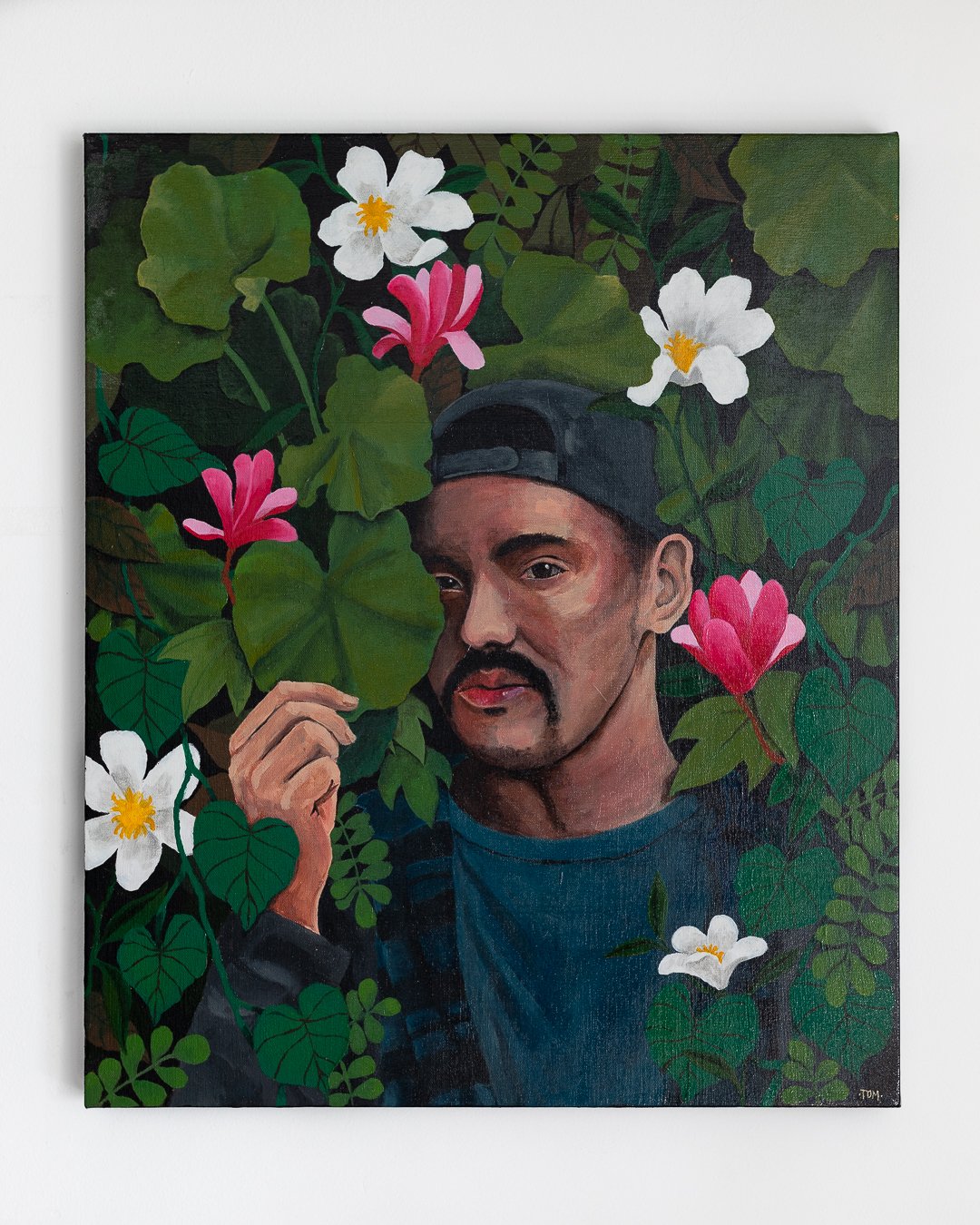 A portrait of a man with a mustache and beard, wearing a backwards baseball cap, surrounded by pink and white flowers and green leaves.