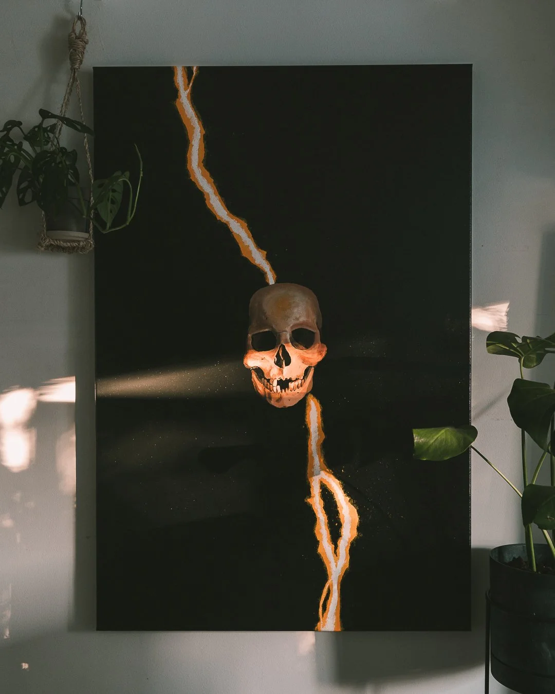 A black canvas painting featuring a human skull with a lightning bolt slicing through it.