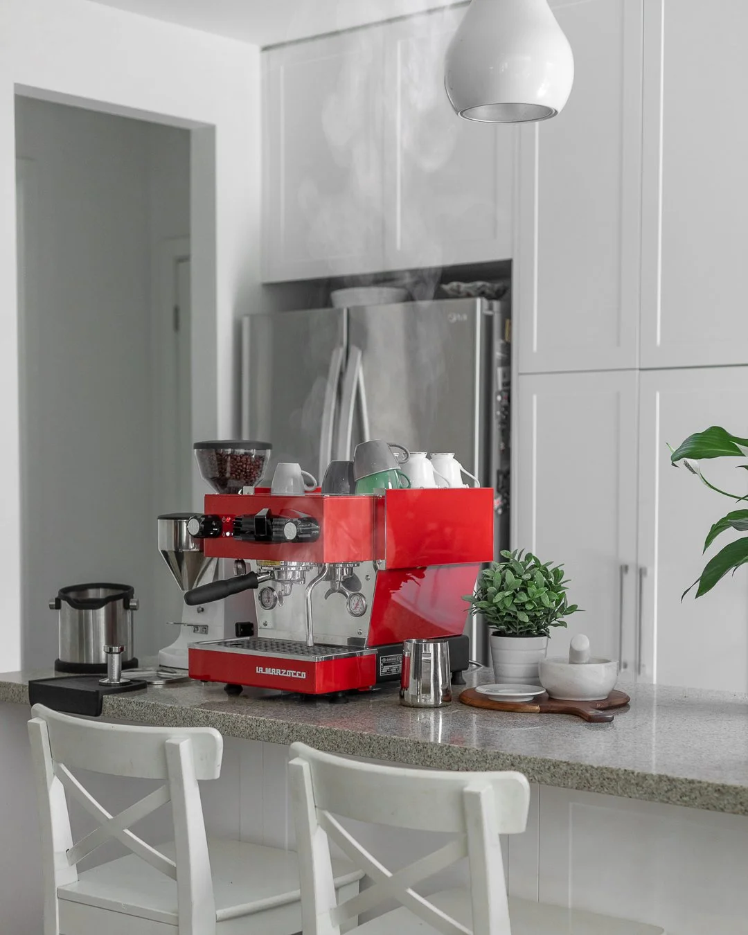 Modern kitchen countertop with a red espresso machine, cups, potted plant, and kitchen accessories.