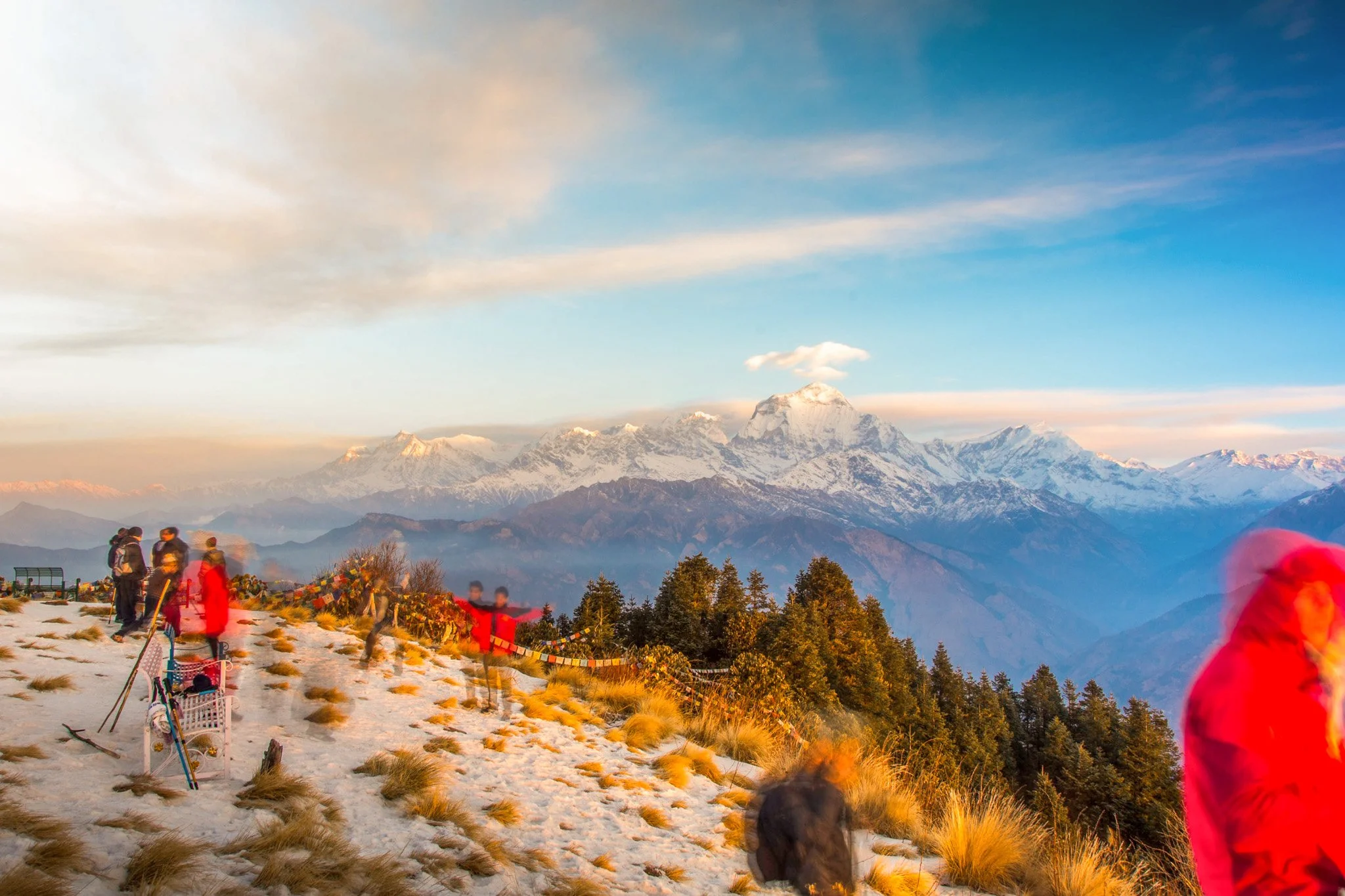 Sunrise view from Poon Hill with trekkers, prayer flags, and Annapurna and Dhaulagiri ranges in the background