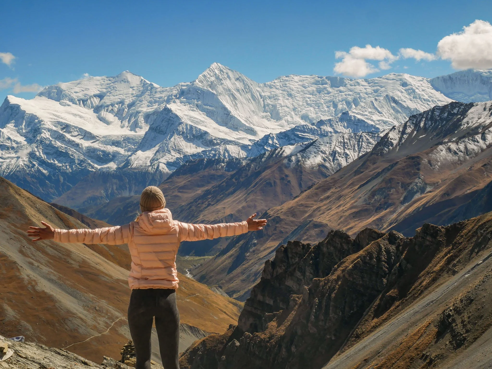 A trekker standing with open arms at a viewpoint in the Annapurna Region, looking out over the valley below.