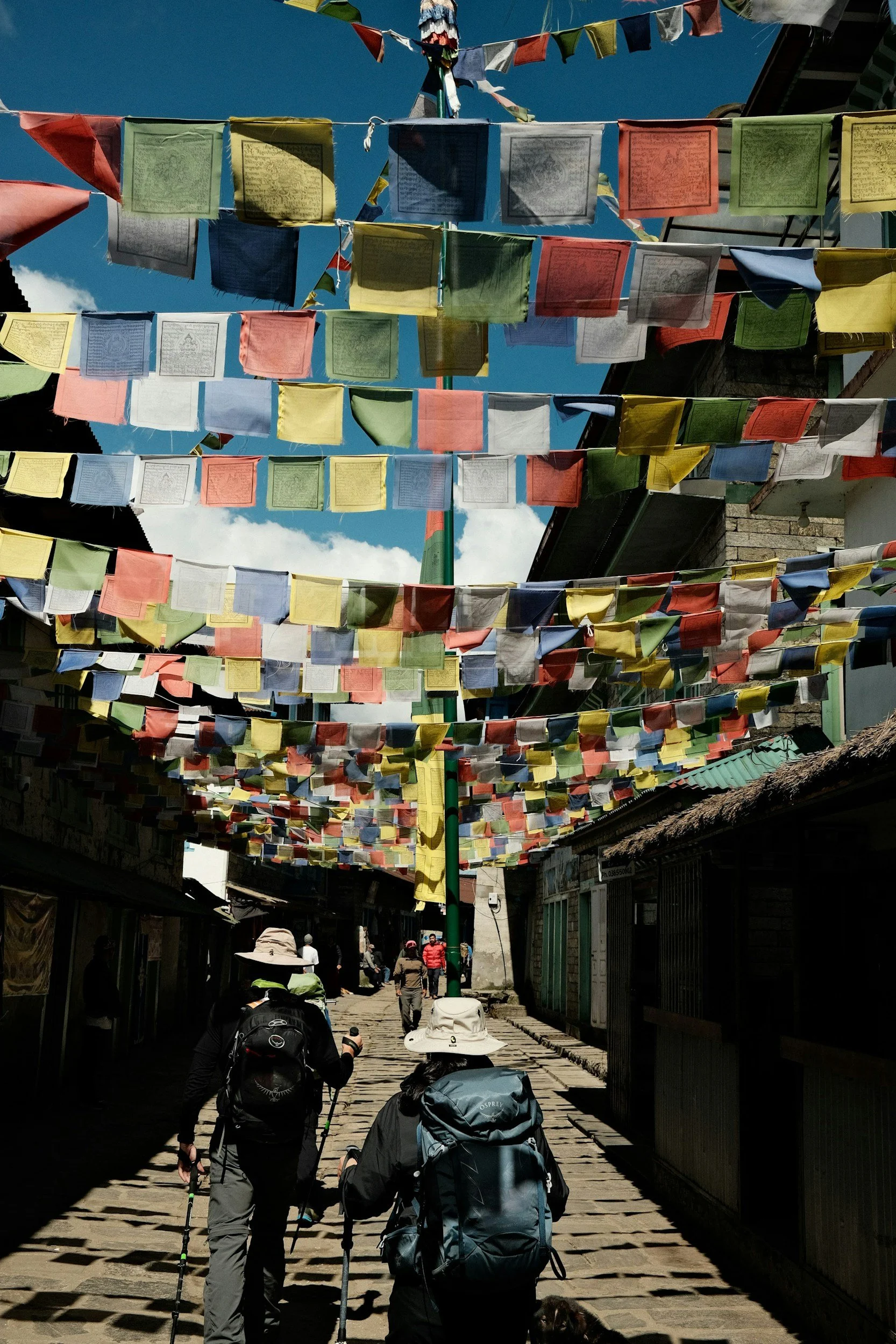 Trekkers walking through Lukla village streets lined with colourful prayer flags at the start of the Everest region trail