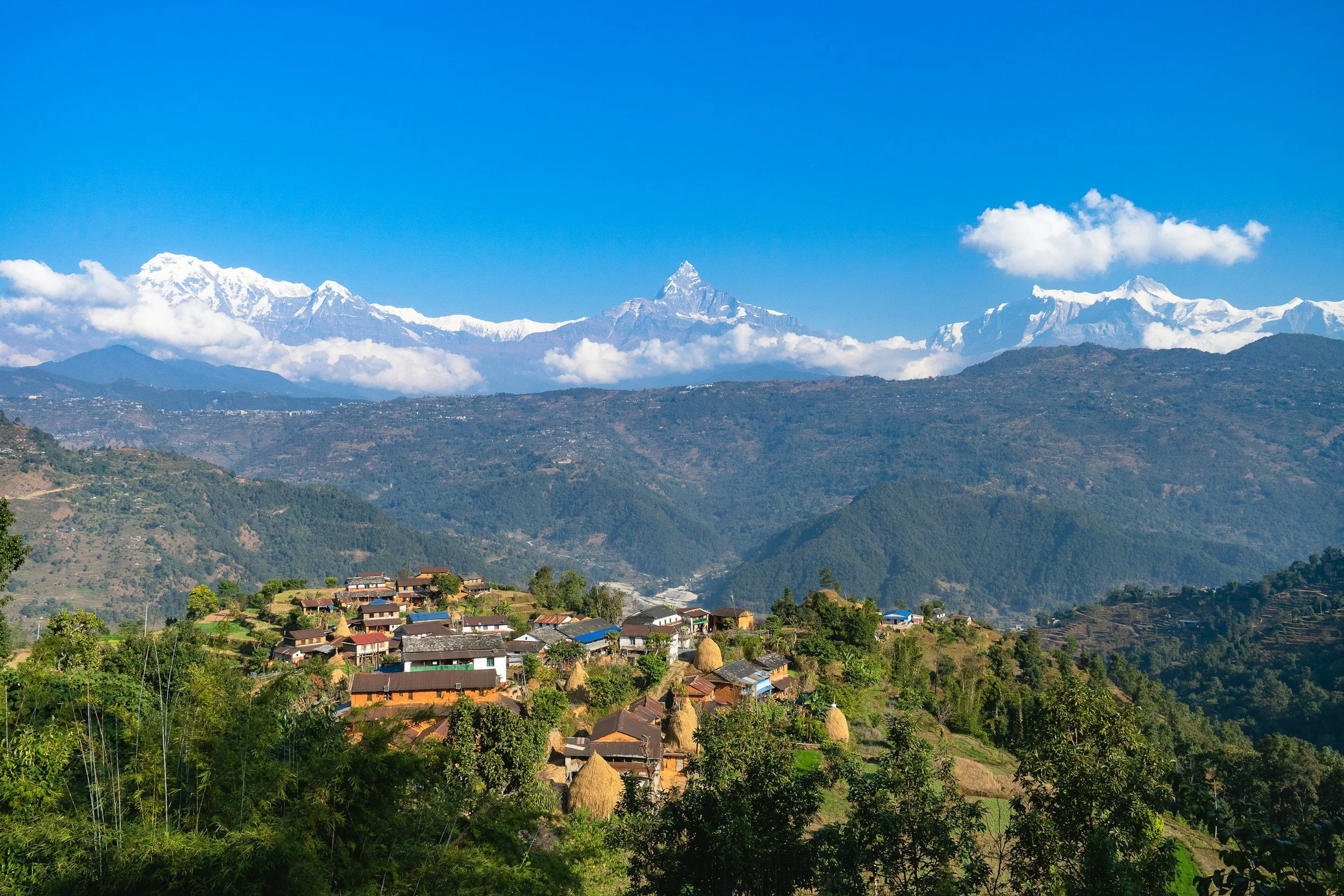 Machhapuchhare standing prominently at the centre of the image, with a Gurung village below and surrounding mountain ranges in Nepal’s Annapurna region