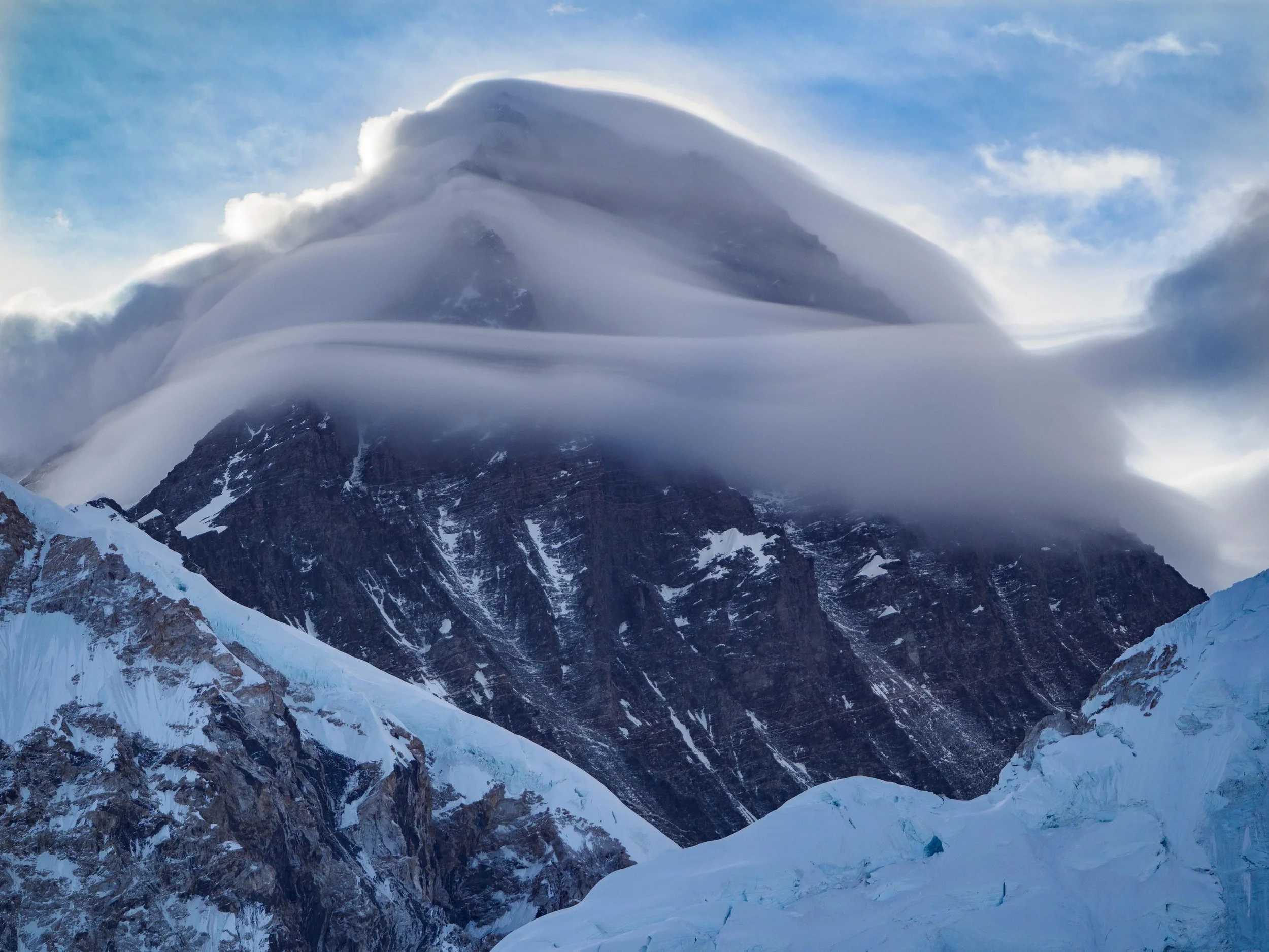 Mount Everest partially covered by a thick blanket of clouds, with the summit hidden and surrounding Himalayan peaks fading into the mist.