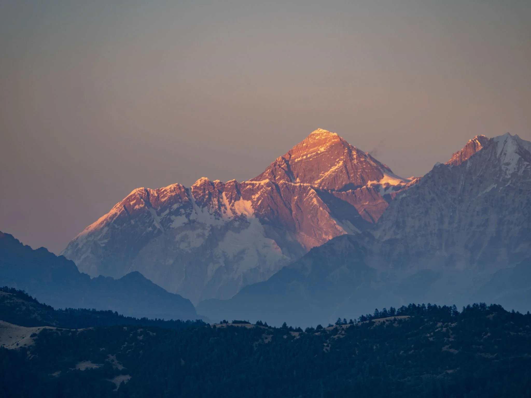 Snow-capped mountain peaks at sunrise with a clear sky in the background.