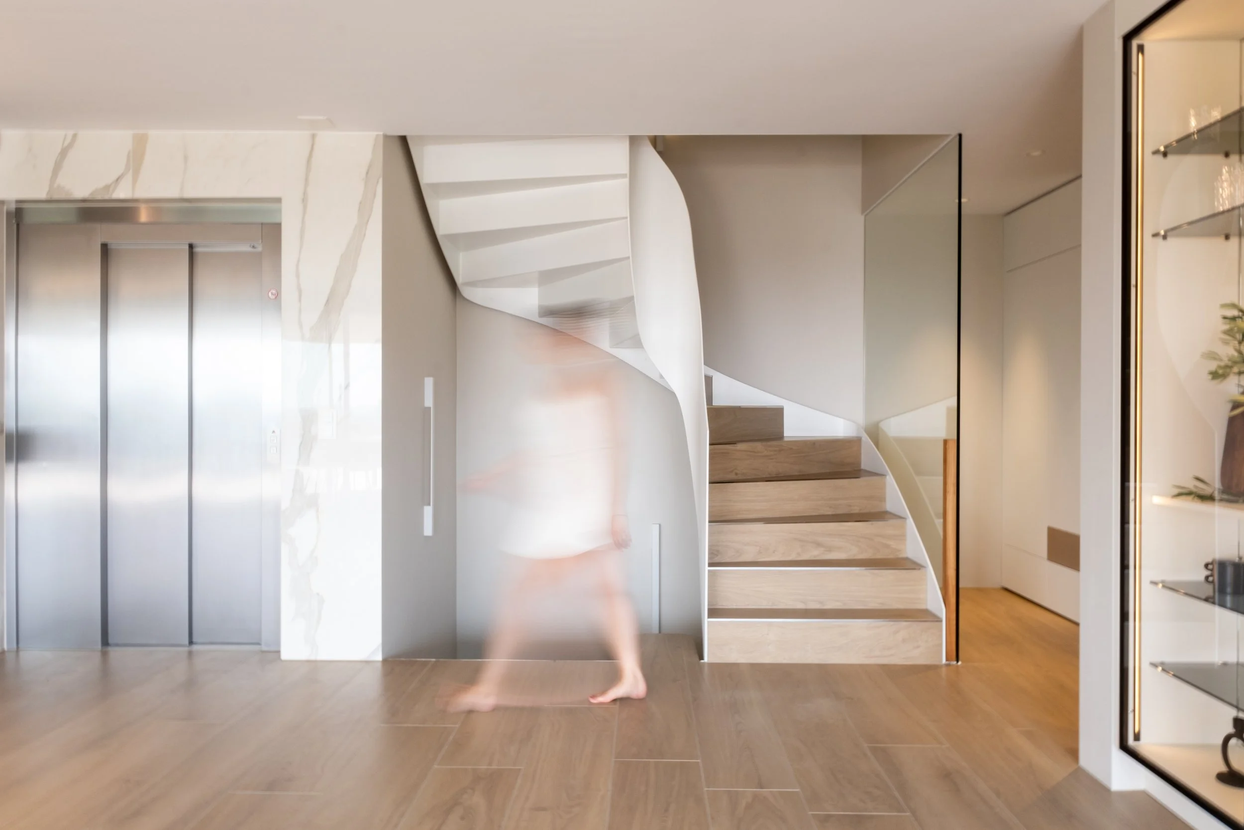 Interior of a modern home with an elevator, a spiral staircase, and a person walking with a blurred effect.